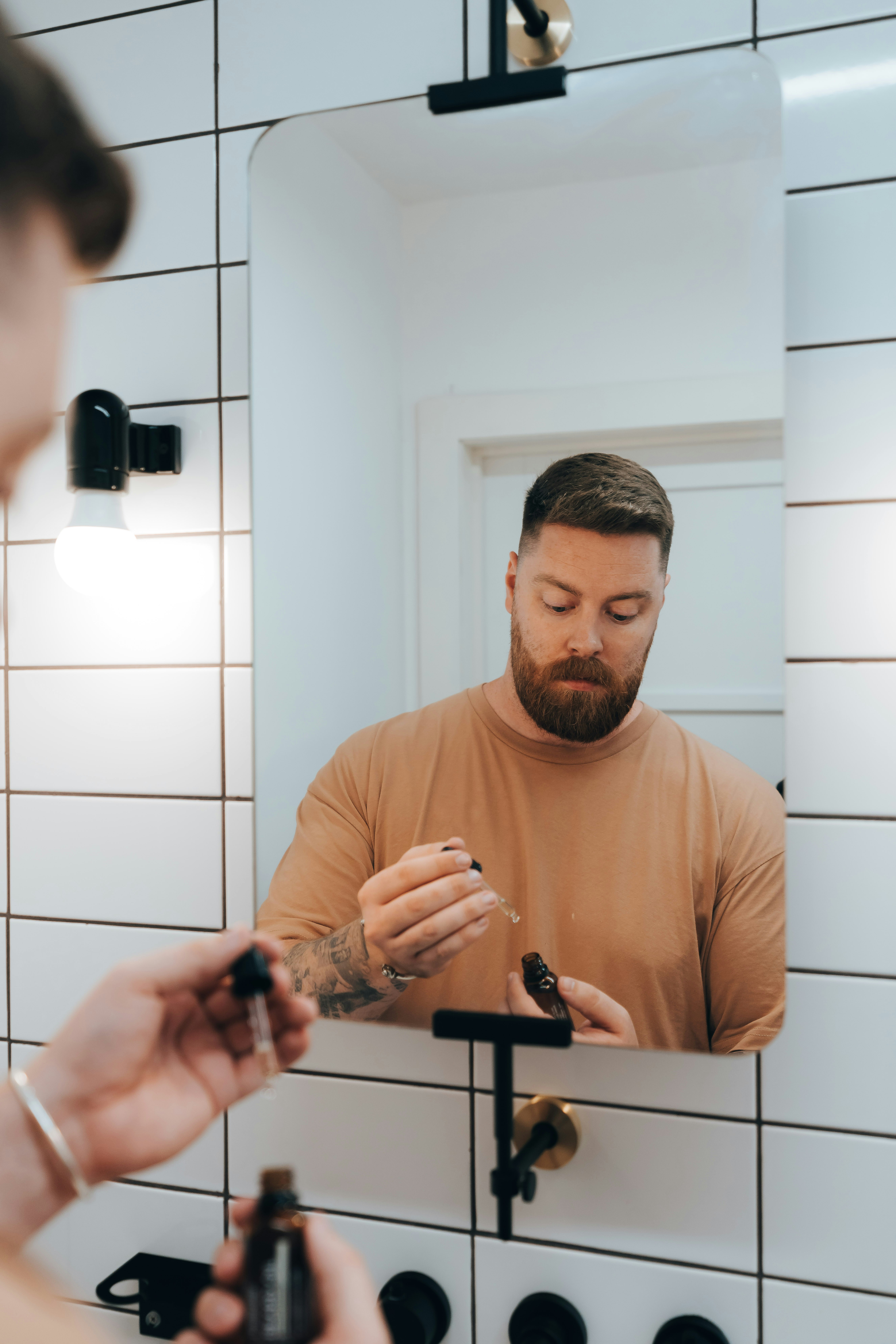 Man applying serum to face in bathroom mirror.