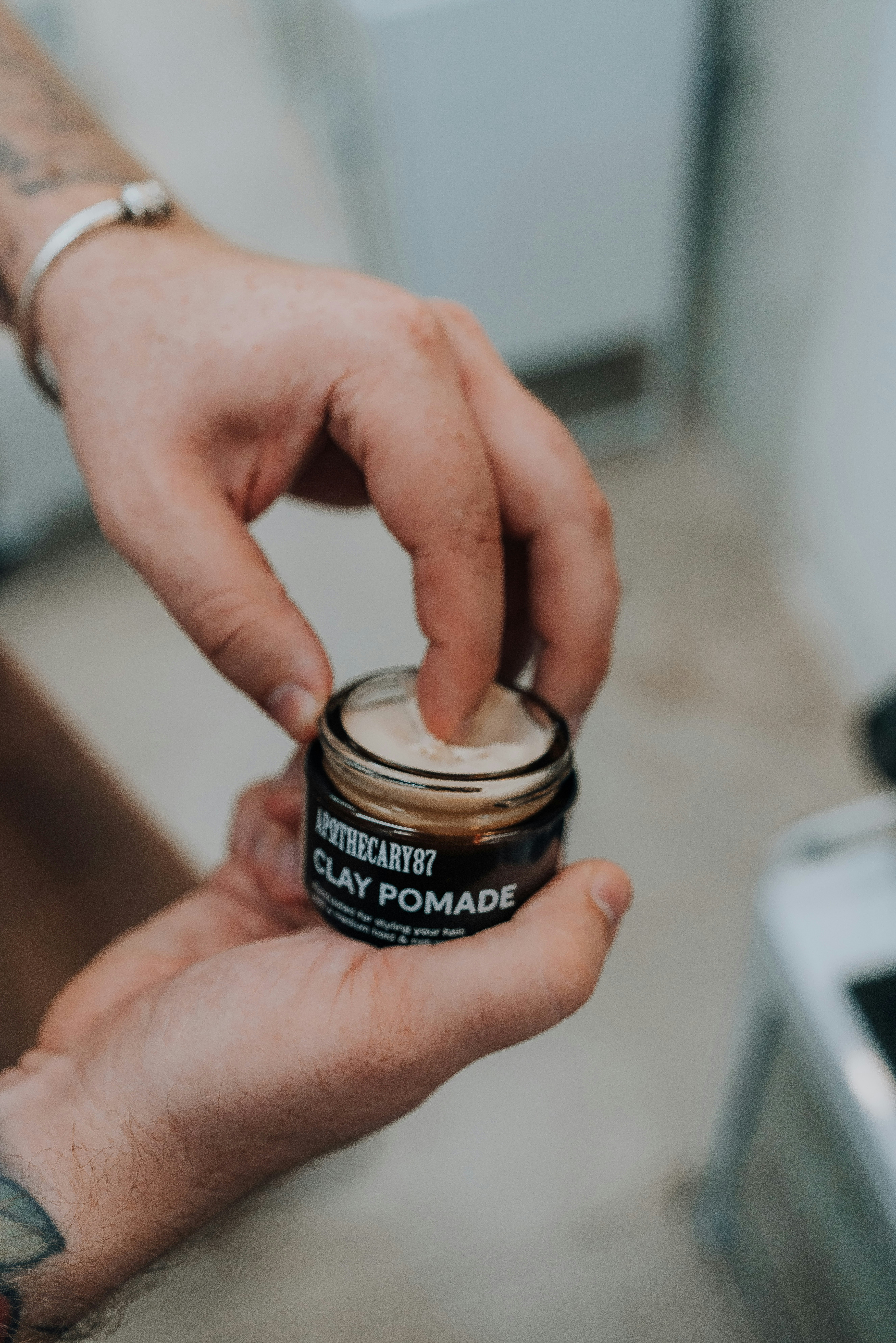 A person scoops clay pomade from a glass jar.