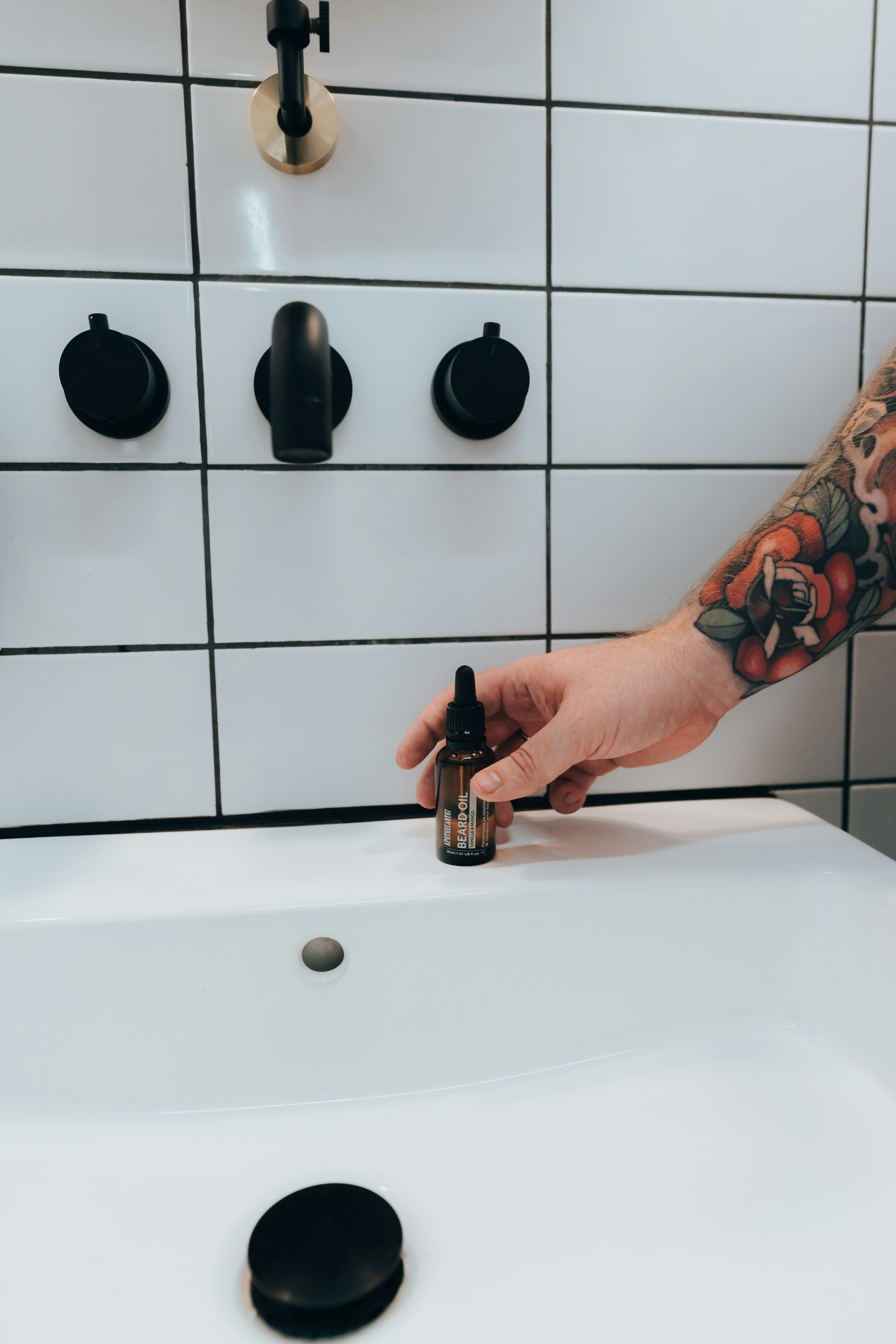 Hand with tattoo reaches for a small bottle.