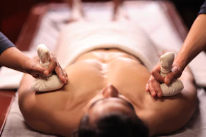 Two hands massaging a person's back with herbal balls