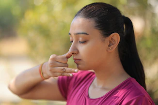 A young woman practicing alternate nostril breathing outdoors.