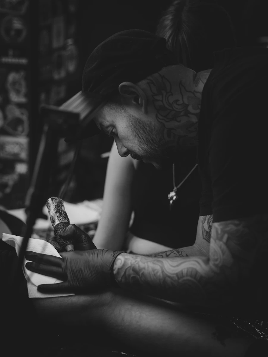Teo leaning in over a client's hand, tattoo machine in hand