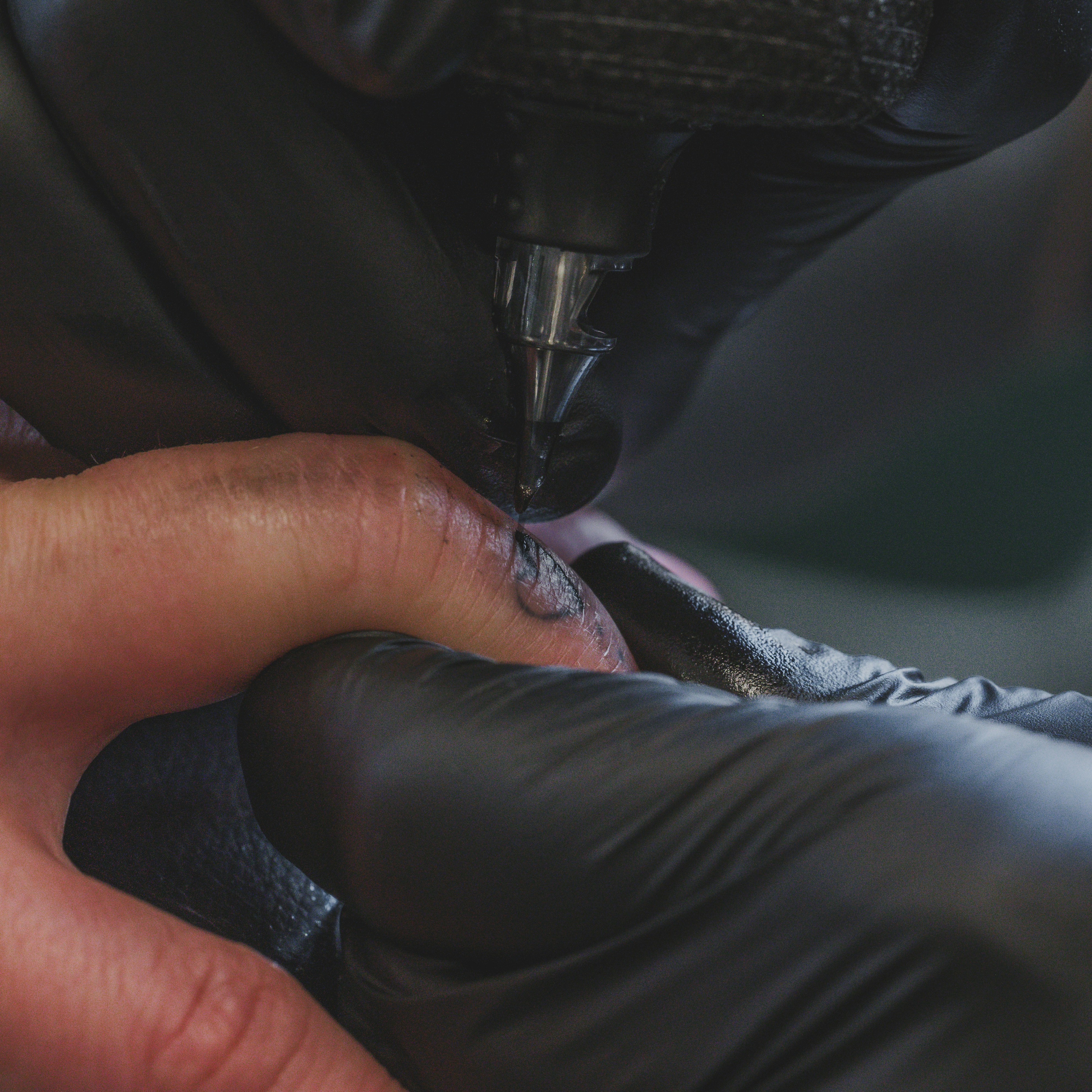 Artist tattooing a hand with black ink.