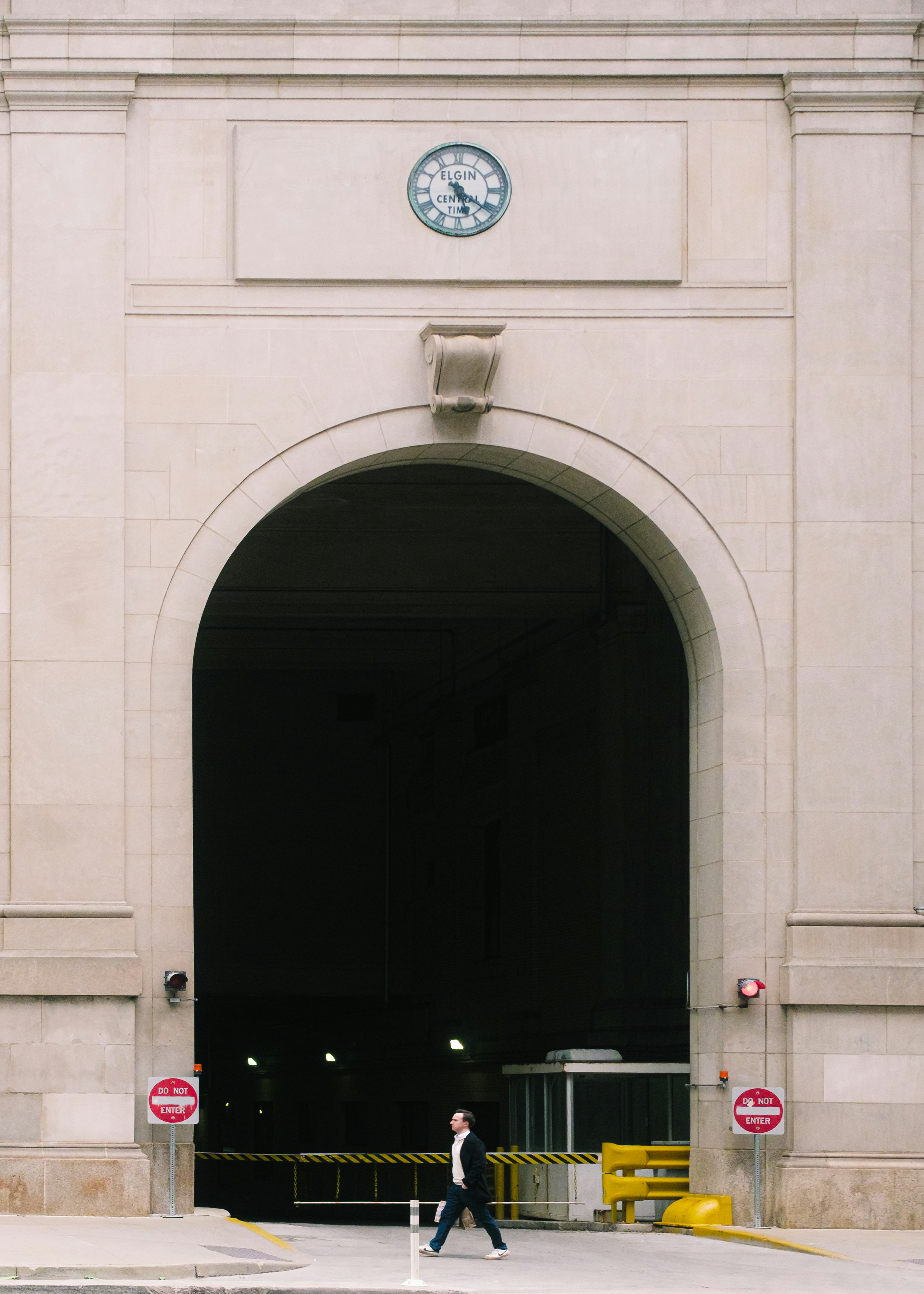 Man walks through large archway with clock above.