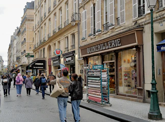 People walk down a parisian street with shops.