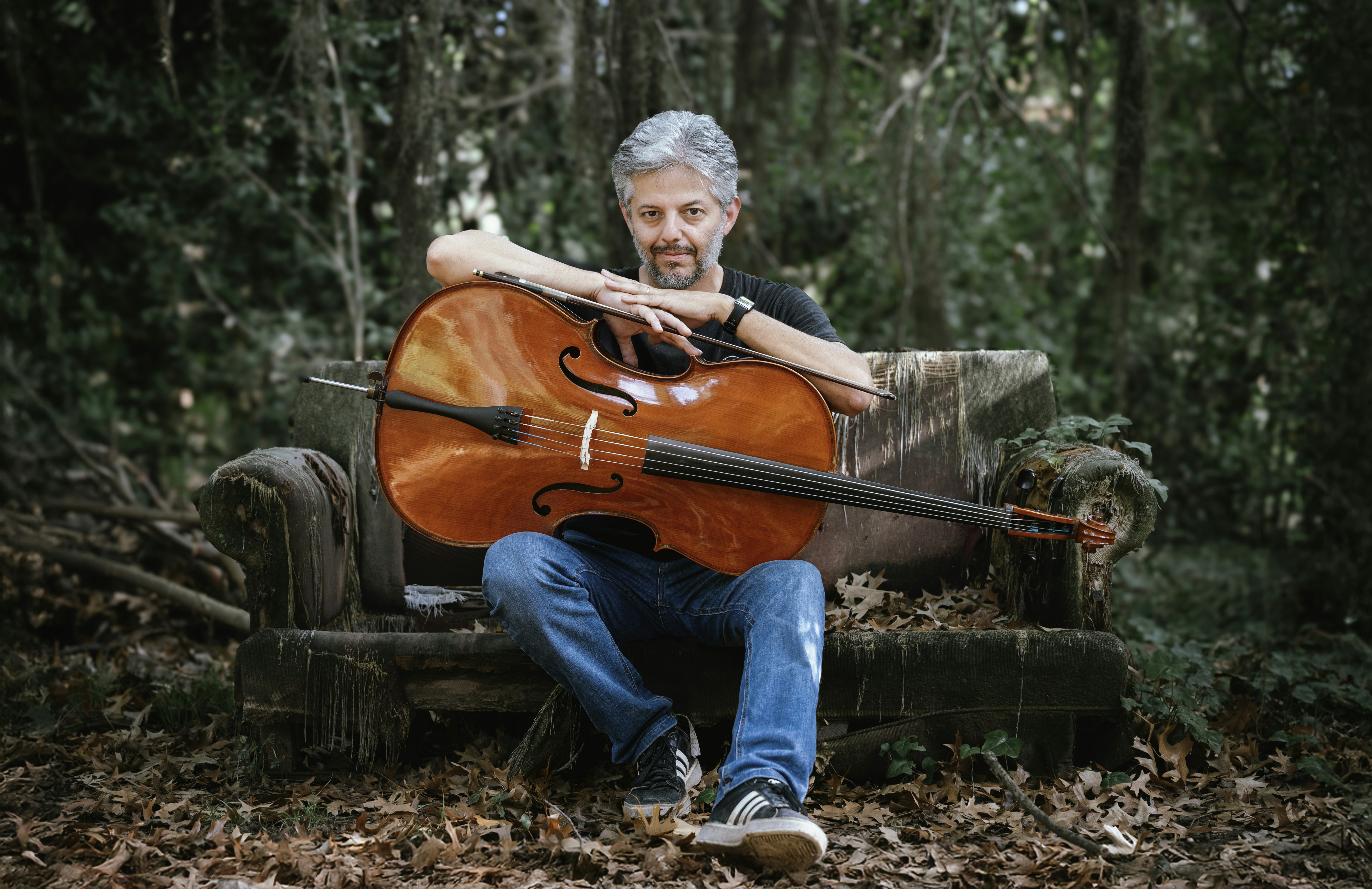 Man with cello sitting on rustic bench in forest