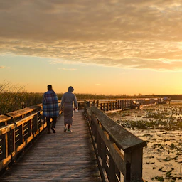 Two people walking with Jesus on a wooden boardwalk at sunset.