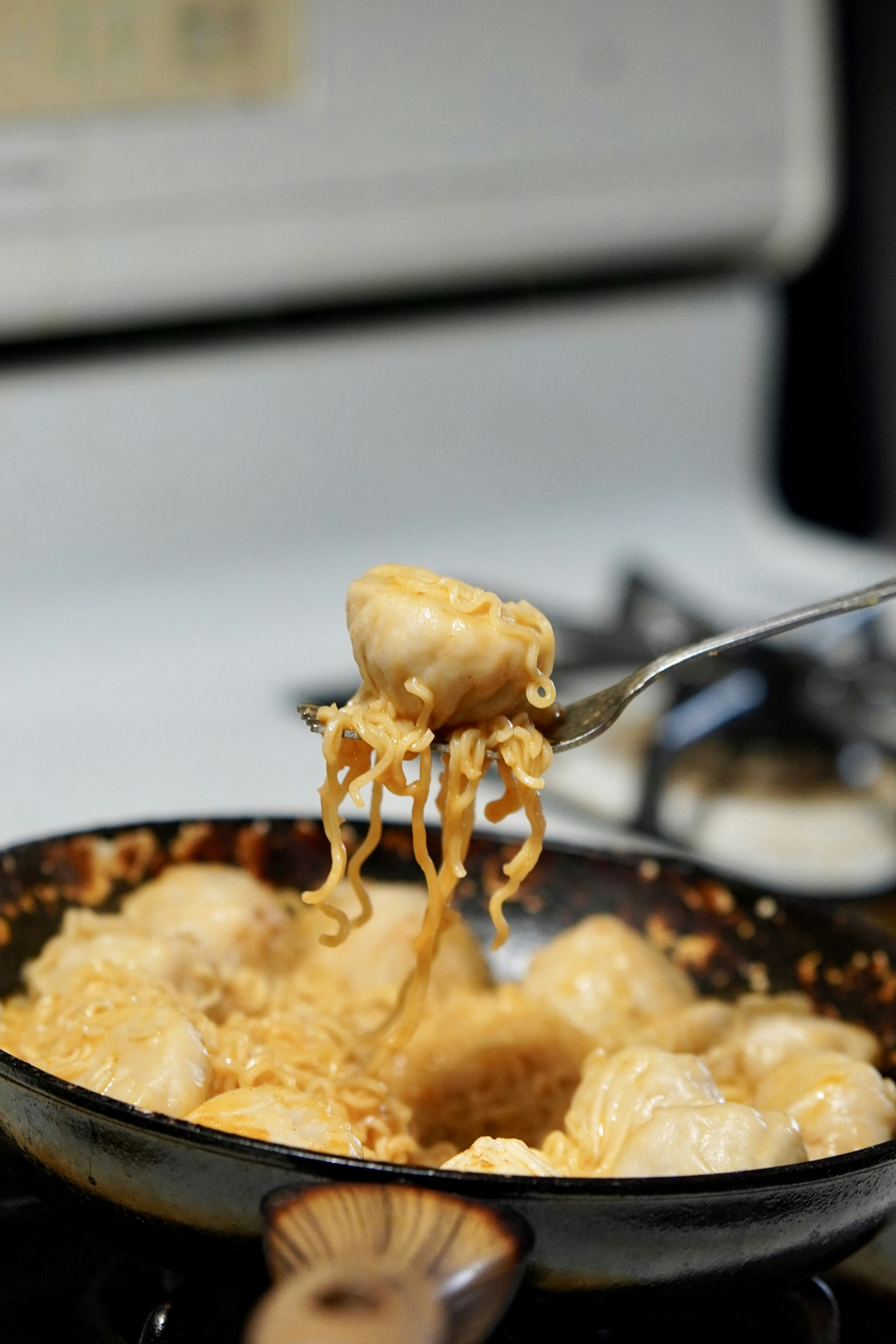 Fork lifting creamy ramen noodles and dumplings from pan