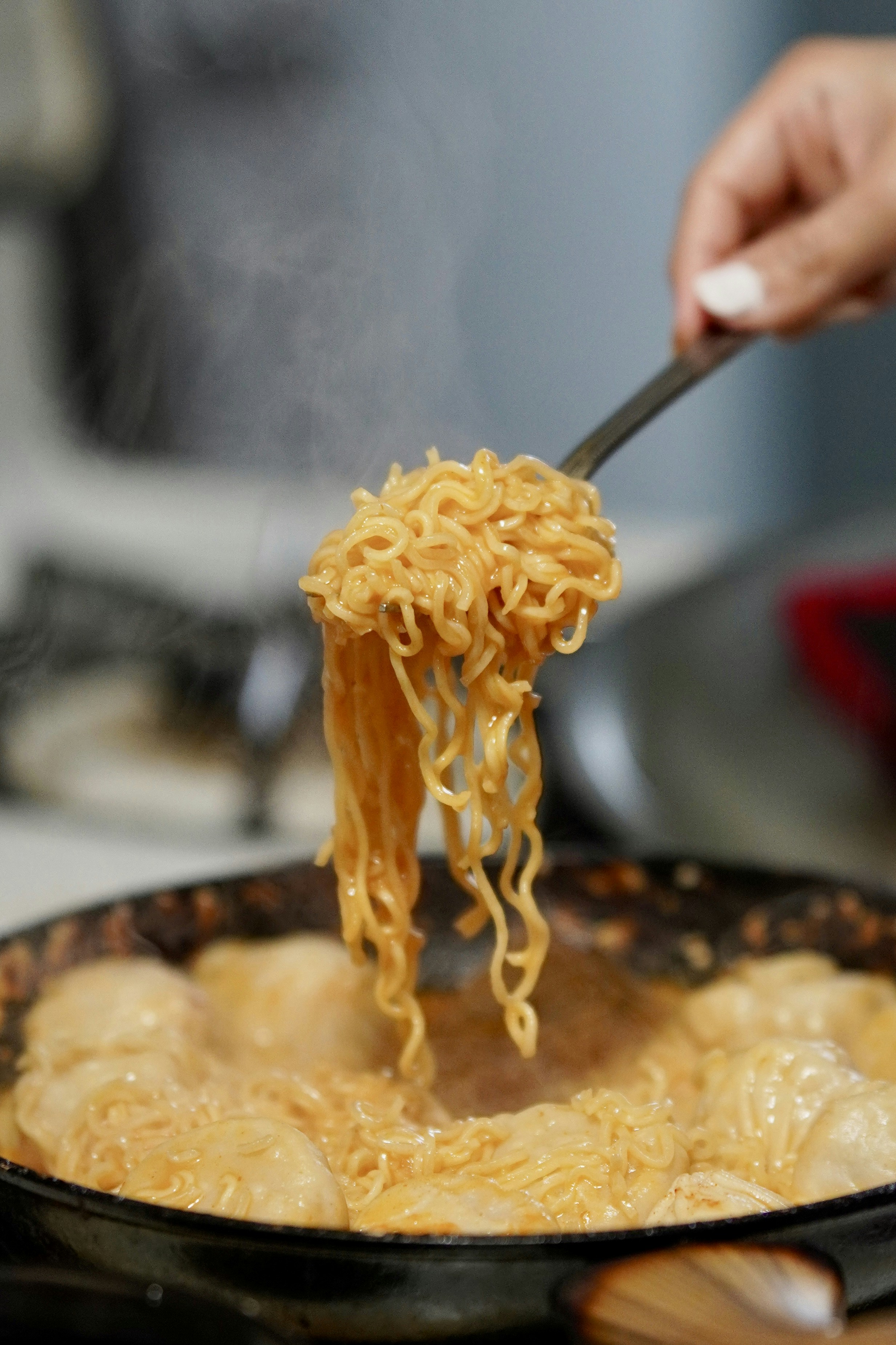 Fork lifting steaming noodles from a pan