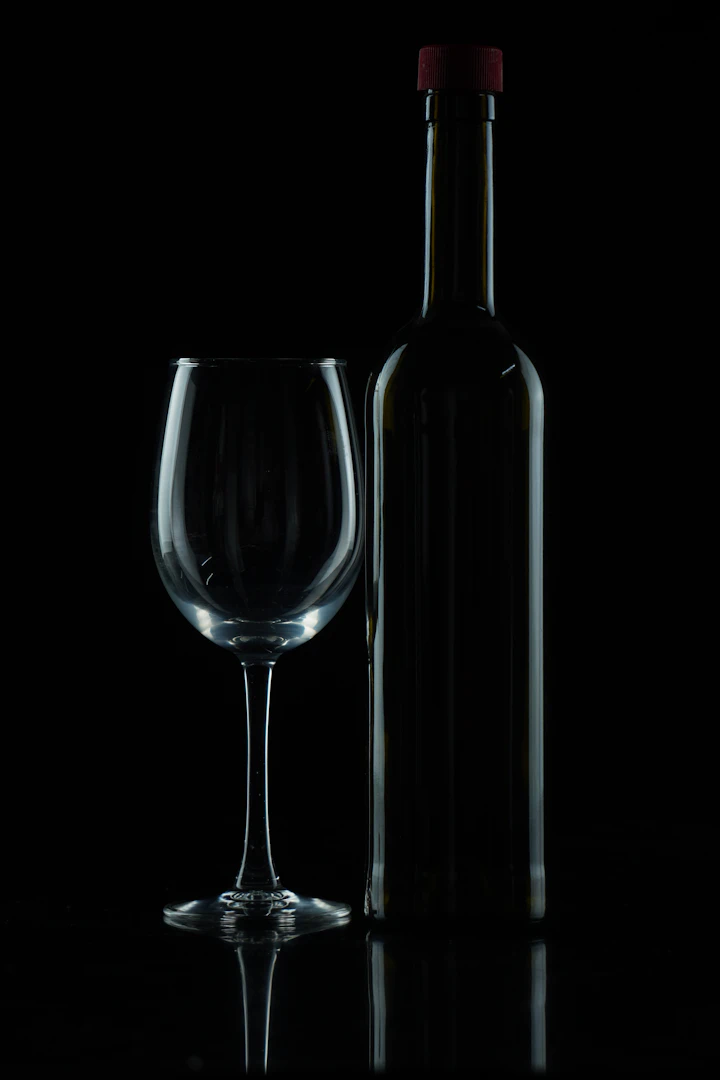 A red wine bottle beside a glass photographed on a black studio background
