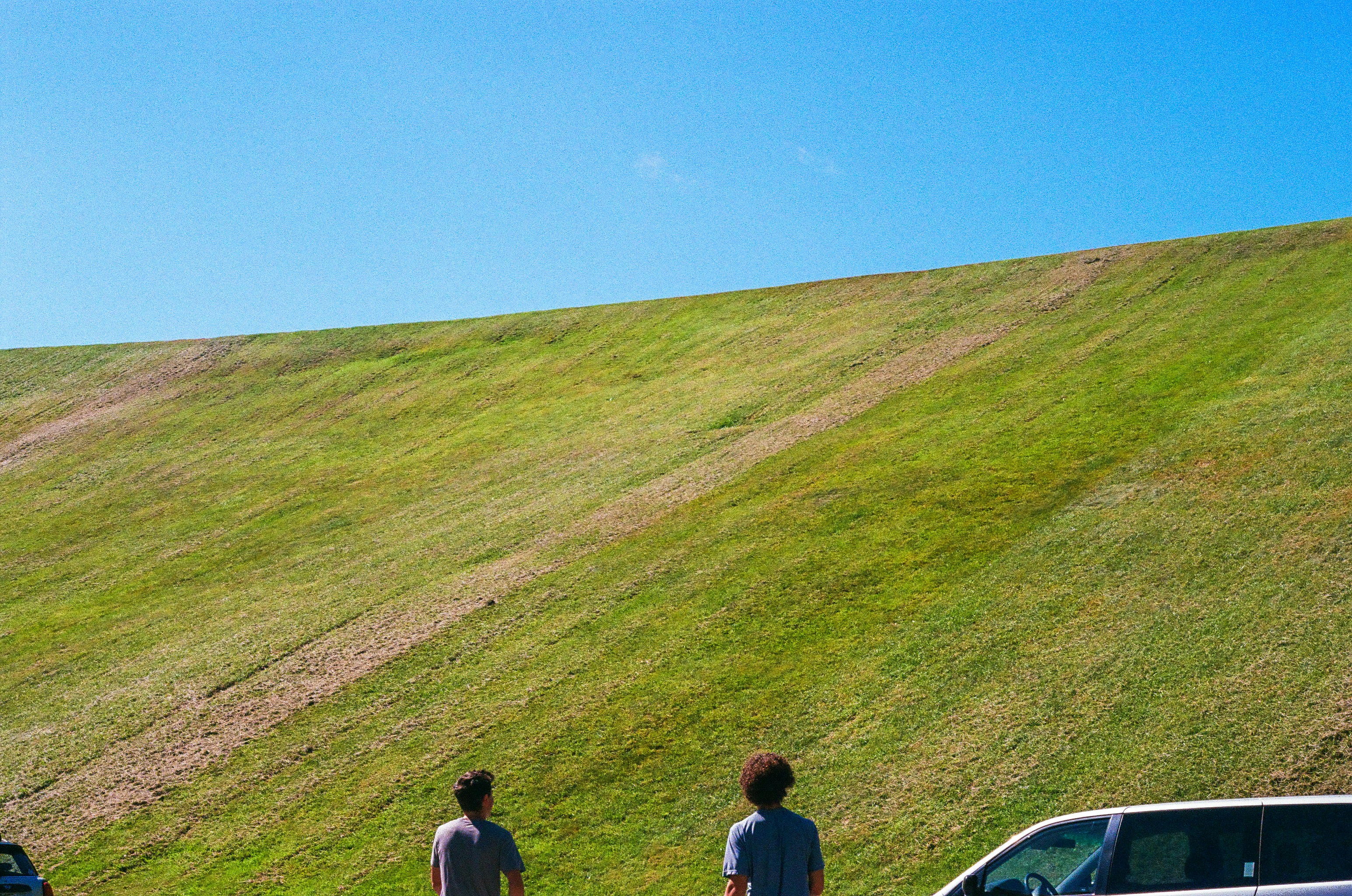 Two people stand before a large grassy hill