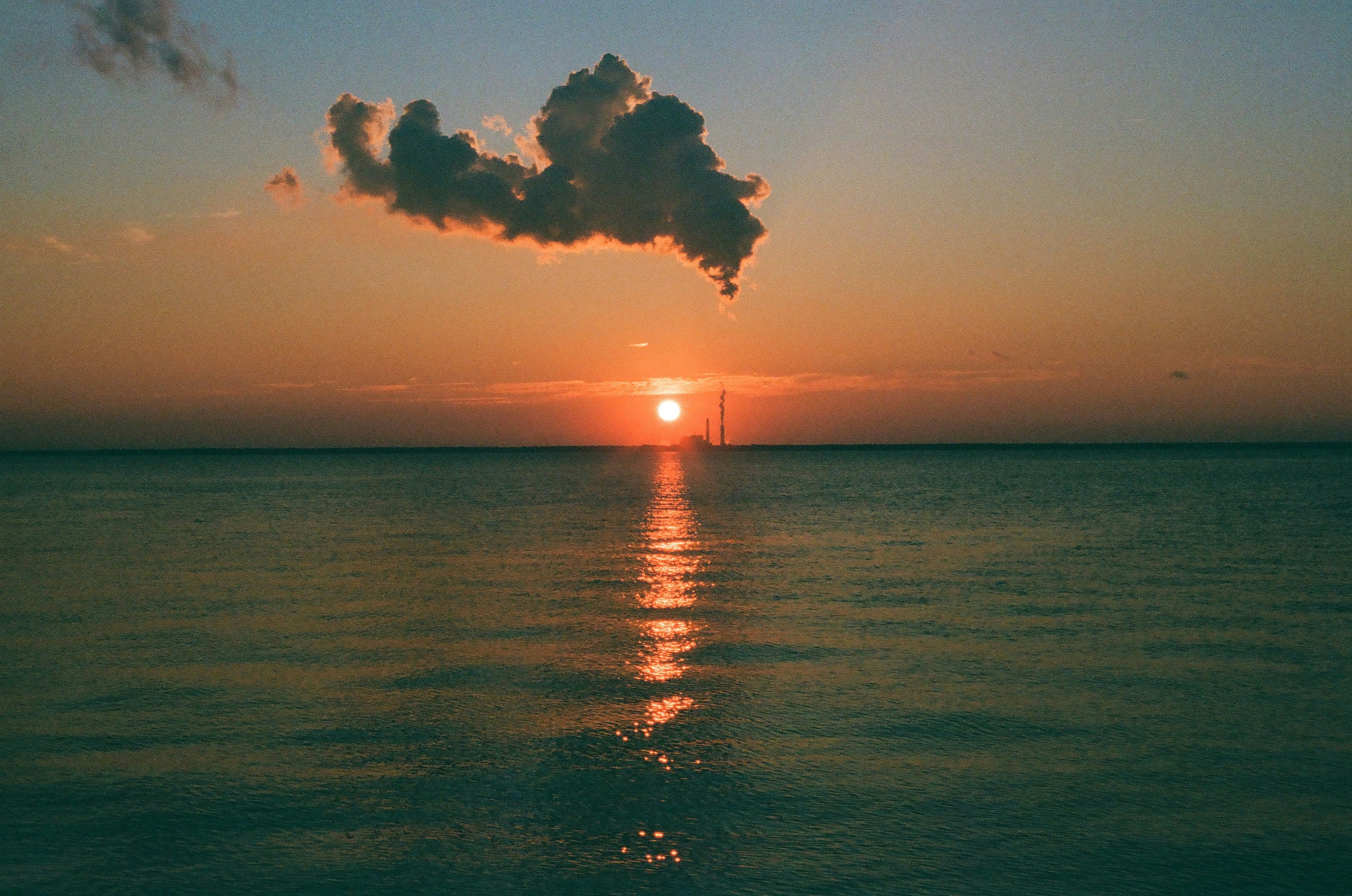 Sunset over a calm ocean with a distant silhouette.