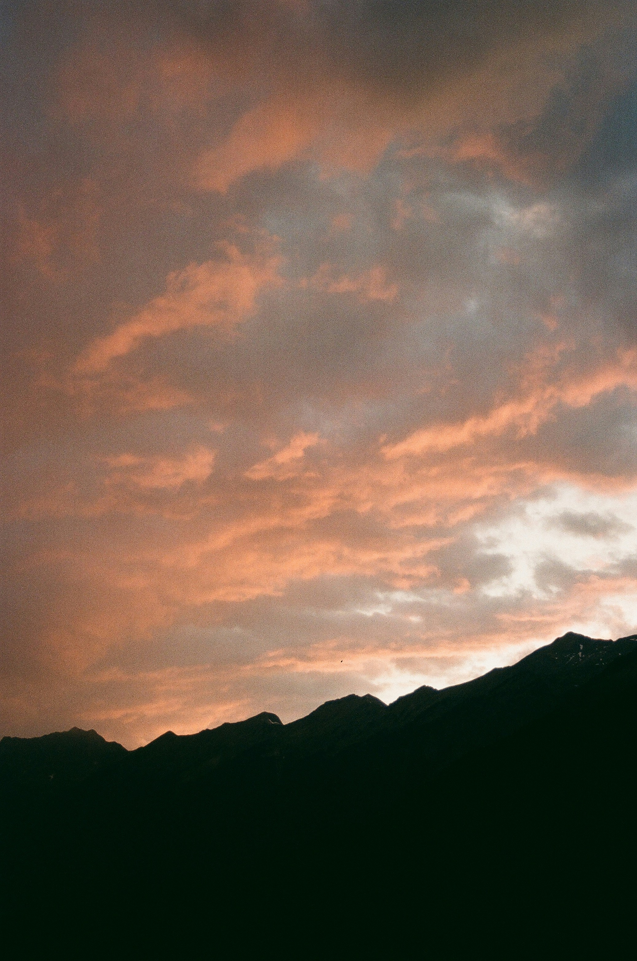 Pink clouds drift over dark mountain silhouette at sunset