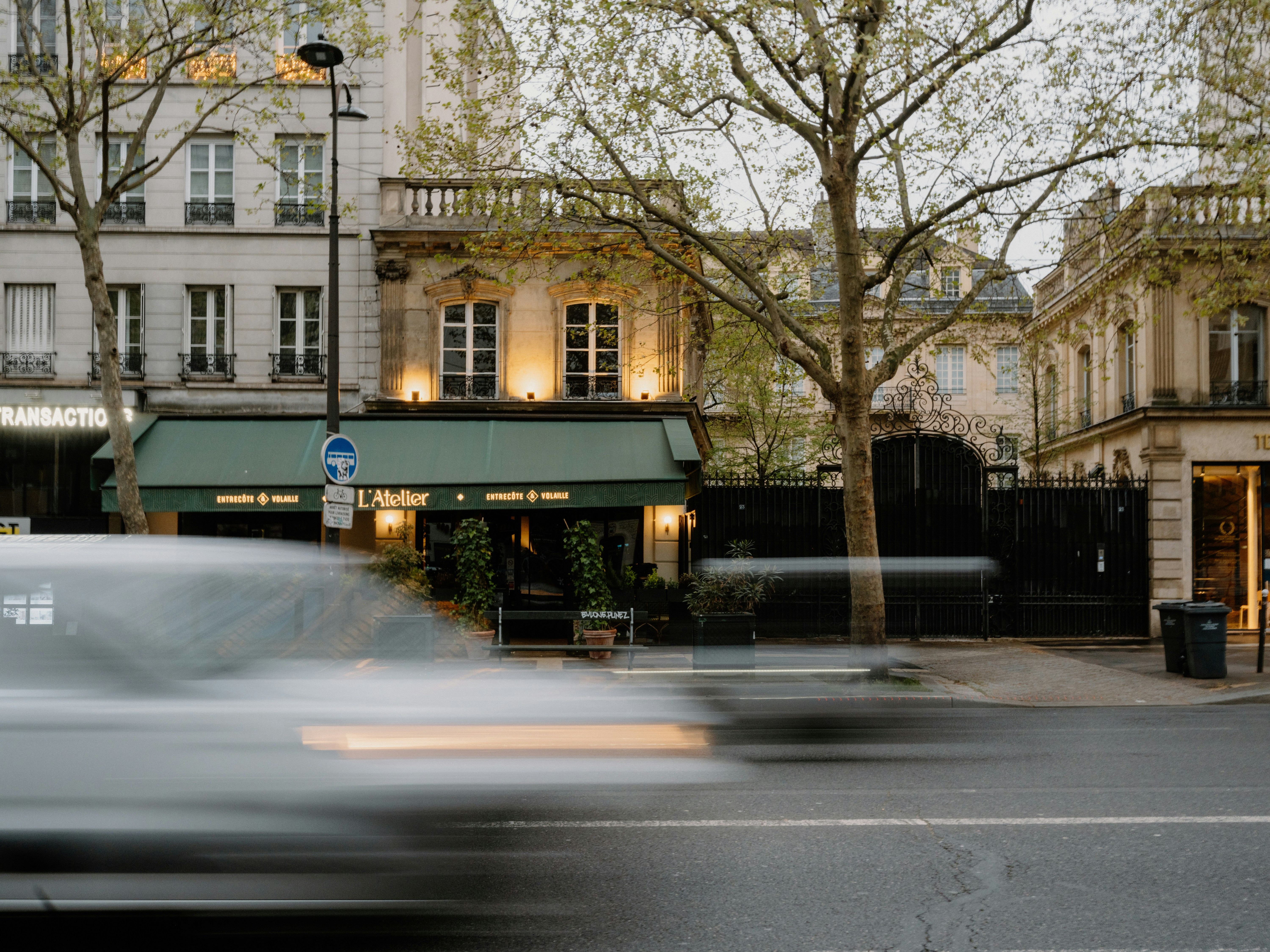 Blurry car passes by a parisian cafe facade.