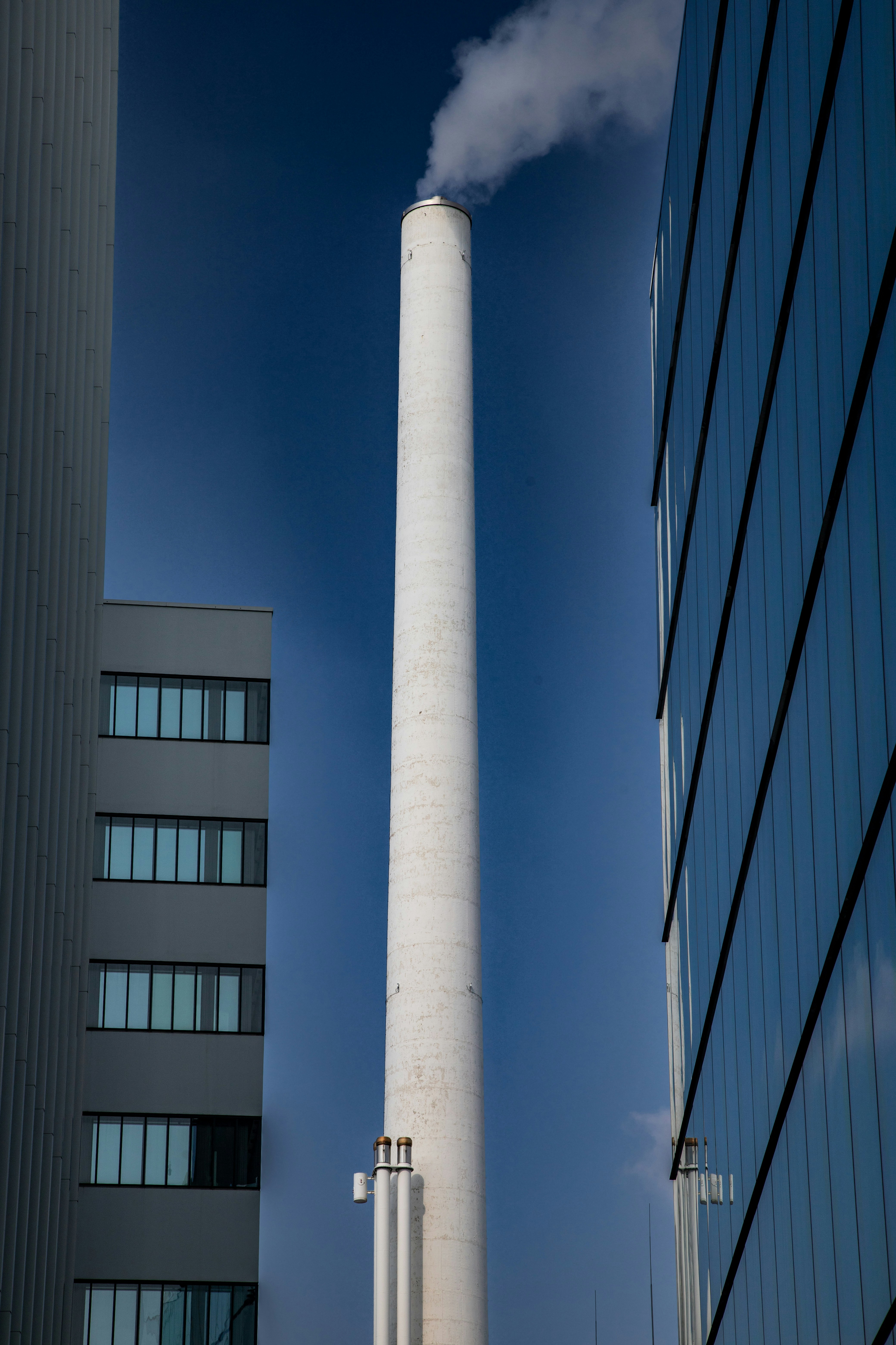 Hoher weißer Schornstein, der Rauch gegen den blauen Himmel ausstößt.