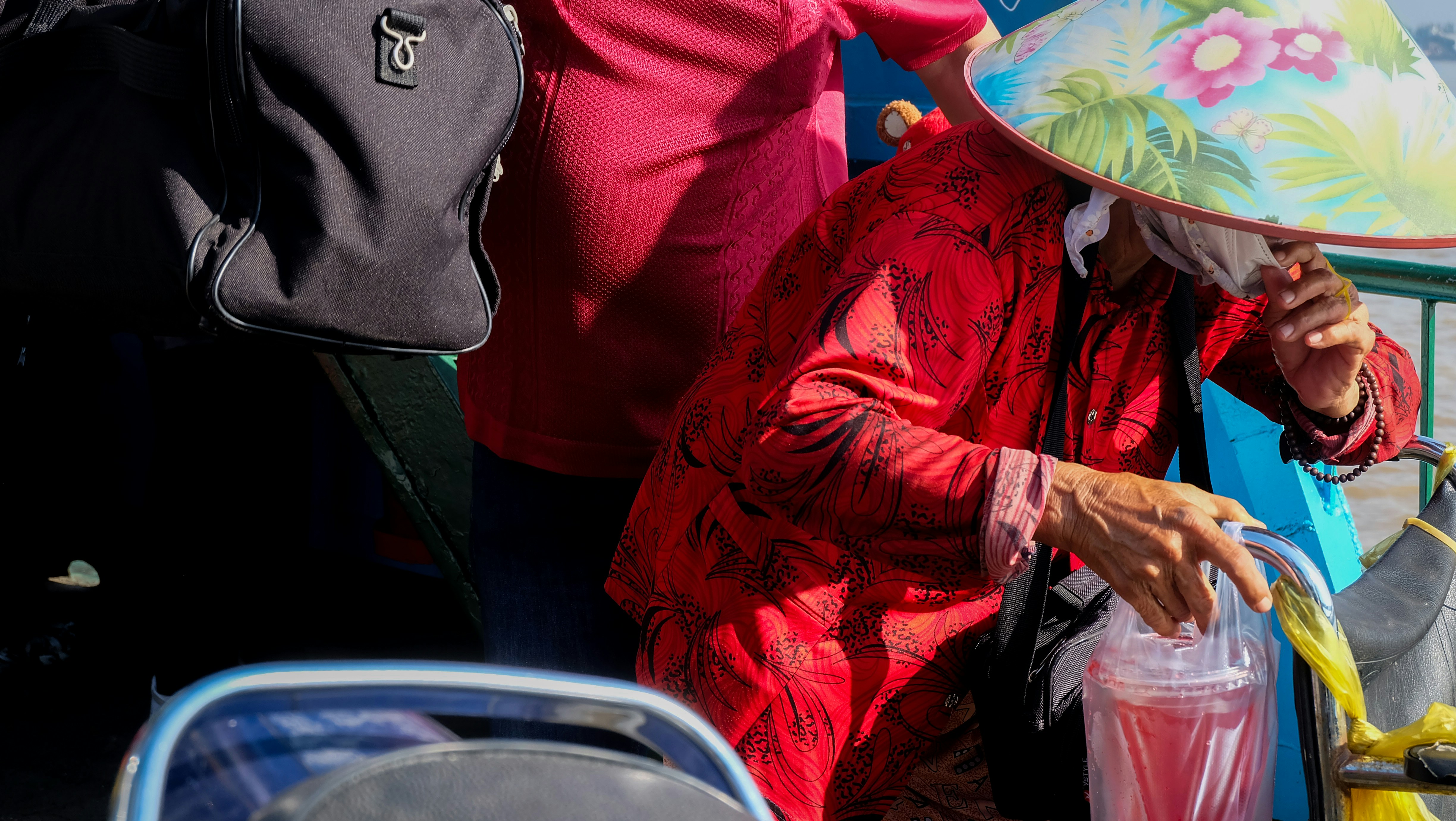 Elderly woman in red pouring drink under conical hat