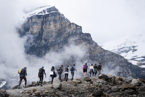 Hikers ascend a rocky mountain trail with snowy peaks.