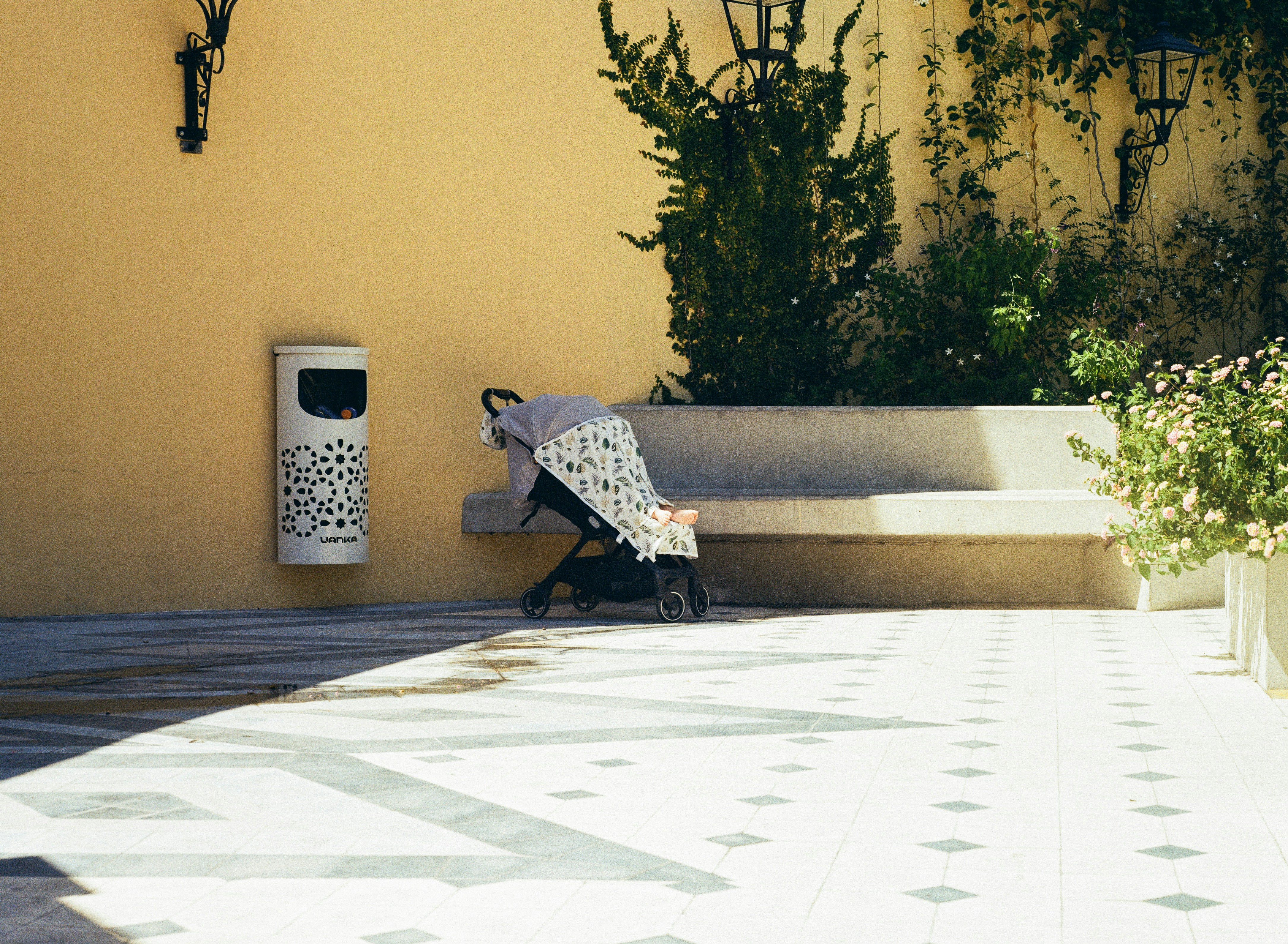A stroller sits on a patterned patio near a bench.