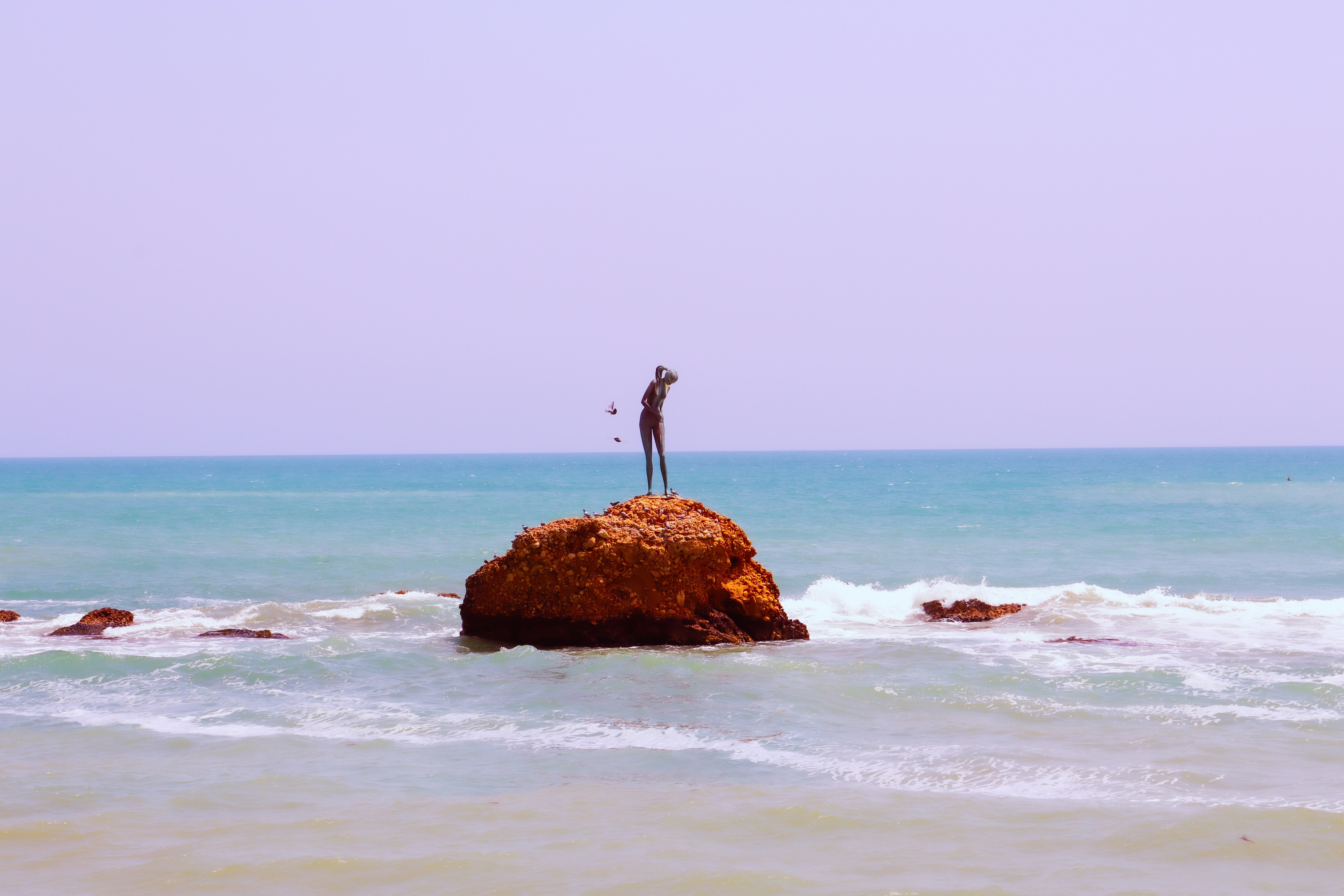 A lone figure stands on a rock in the ocean.