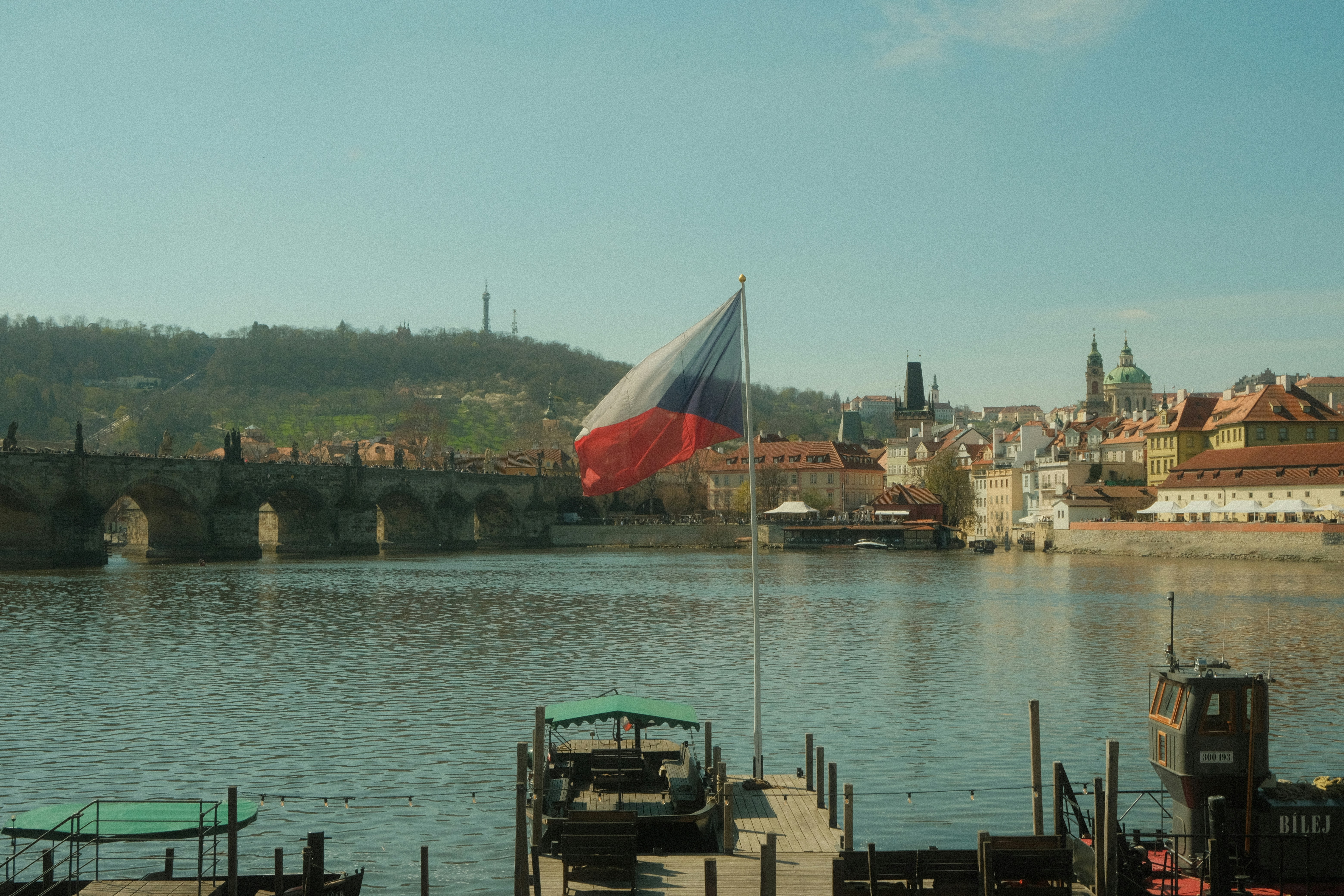 Czech flag waving over a river with city skyline.