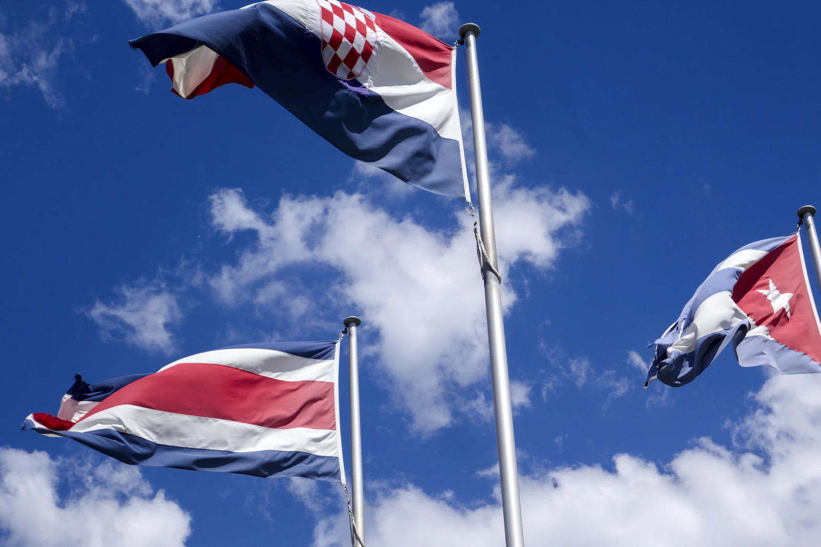 Three international flags against a blue sky