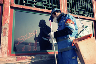 Worker in blue uniform cleans window with spray bottle