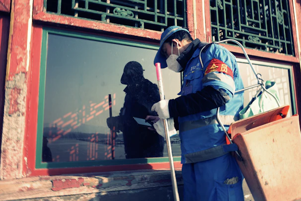 Worker in blue uniform cleans window with spray bottle