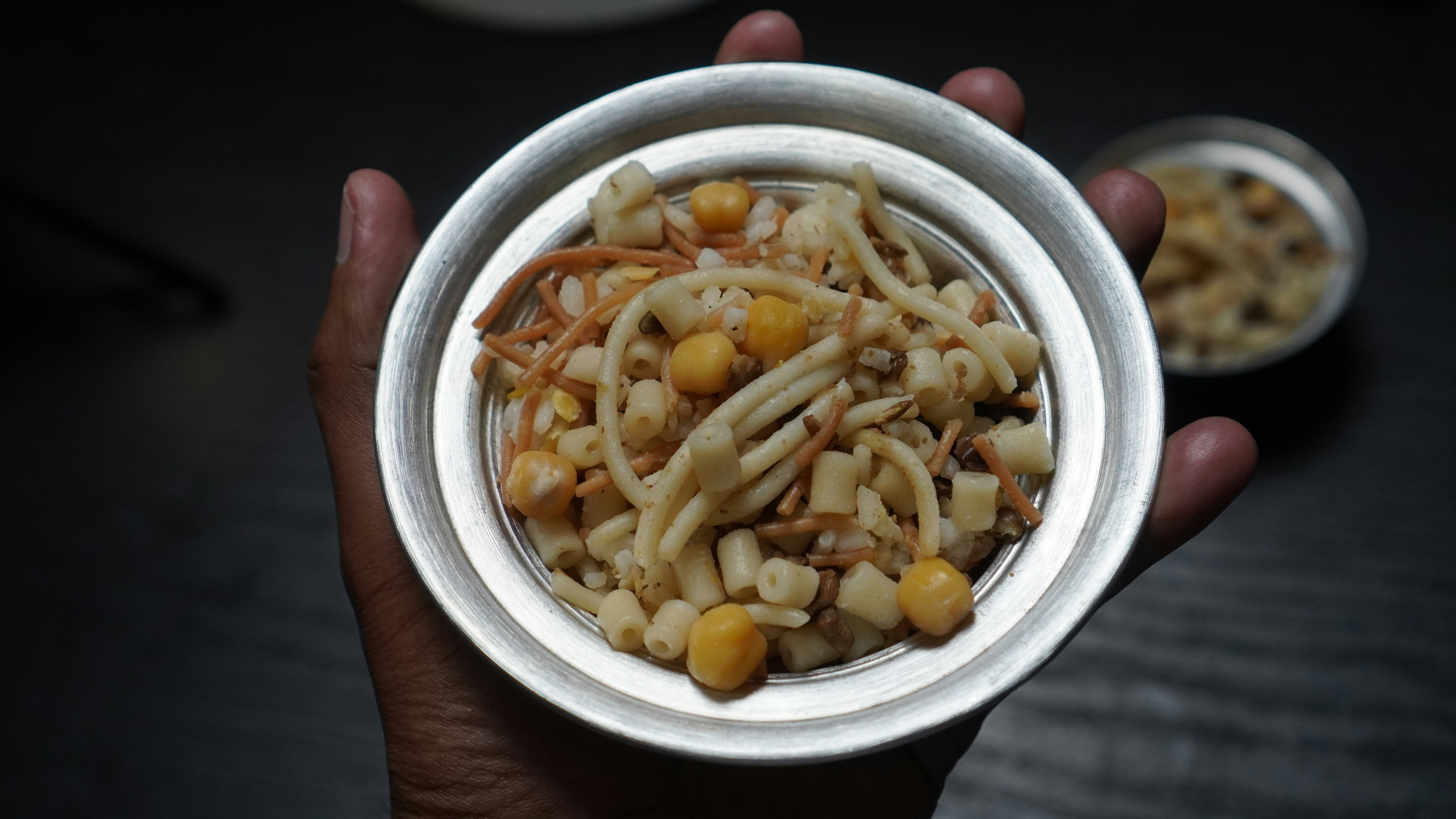 A hand holding a bowl of pasta and chickpeas