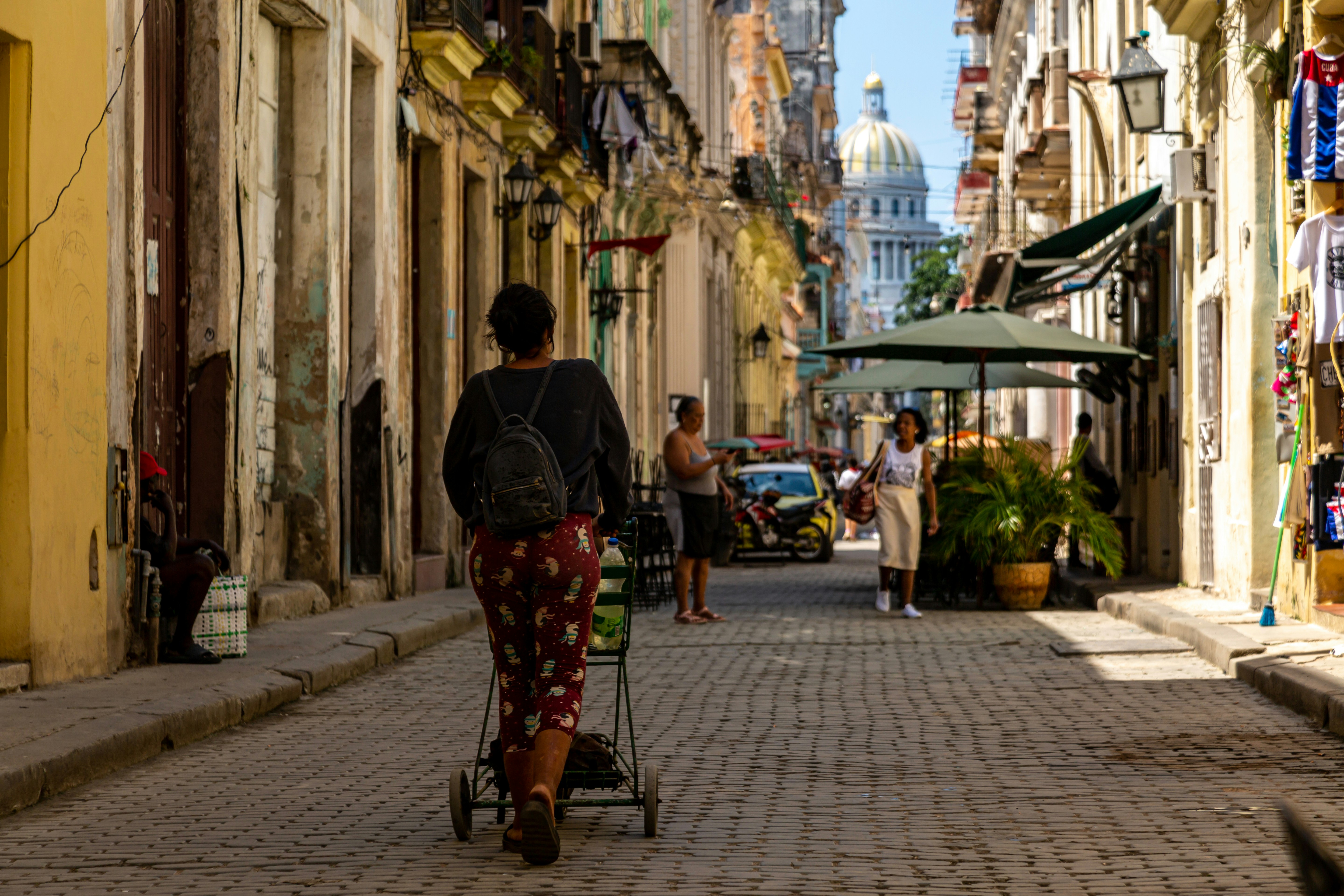 Une femme tire un chariot sur une rue pavée avec un dôme.