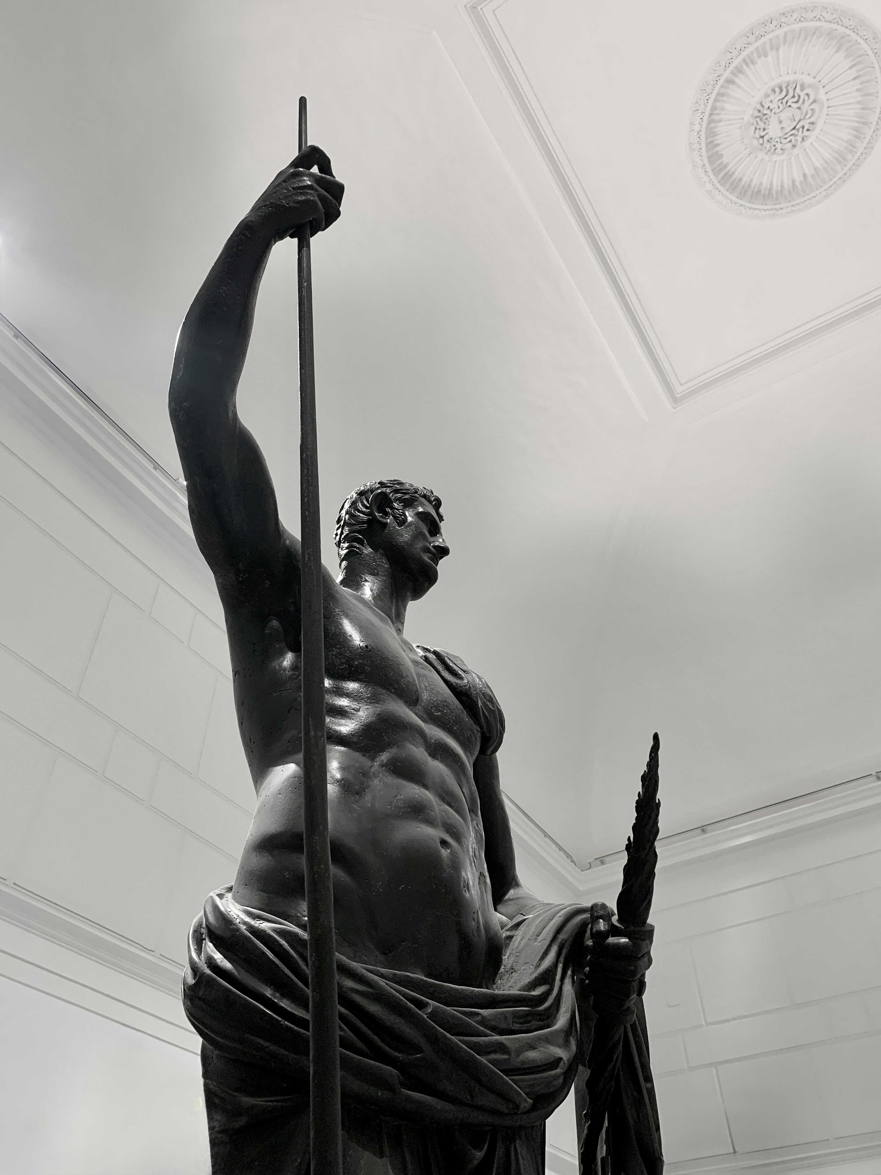Una estatua de bronce de un hombre musculoso sosteniendo una lanza