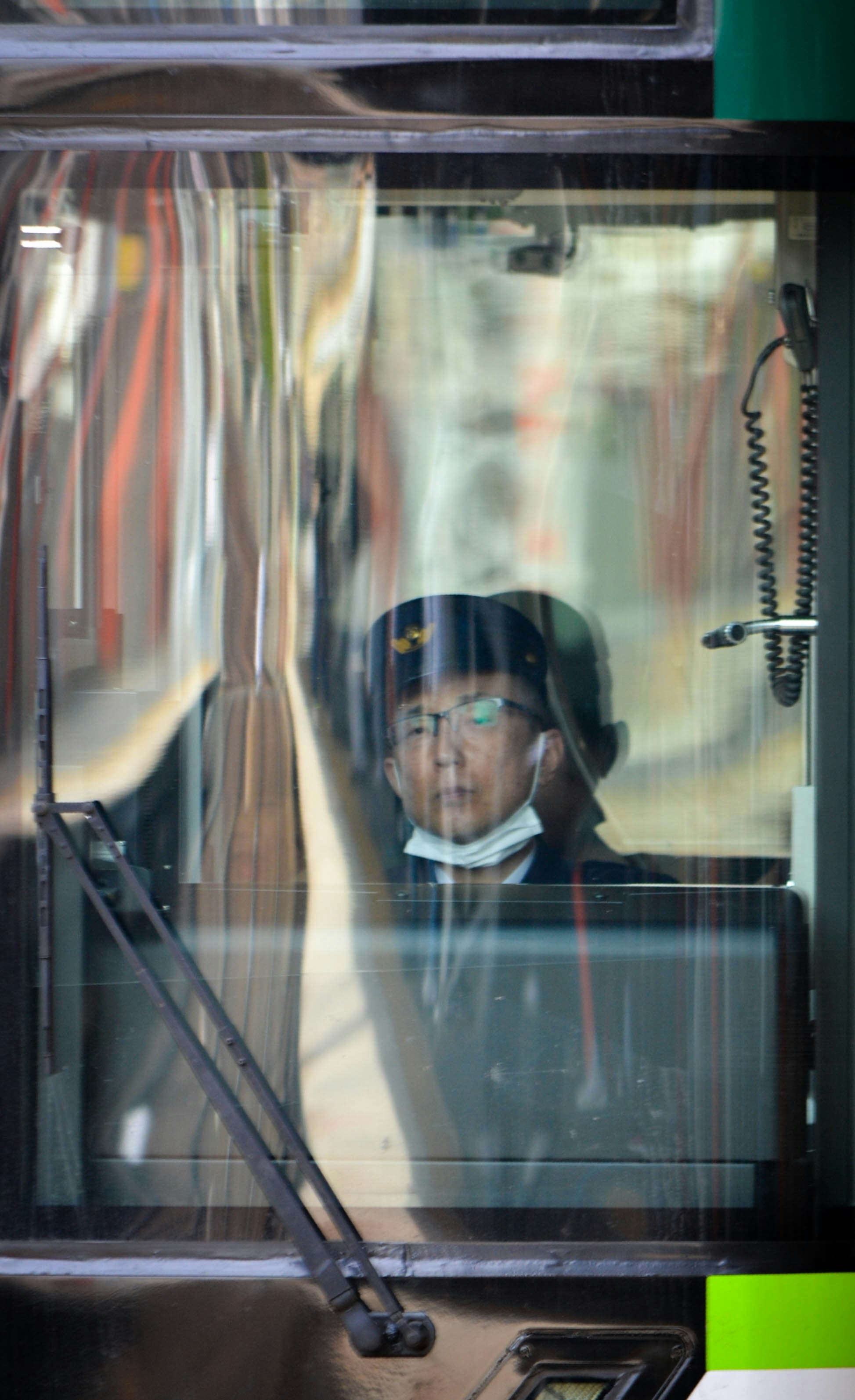 Bus driver wearing glasses and mask looks through the windshield.