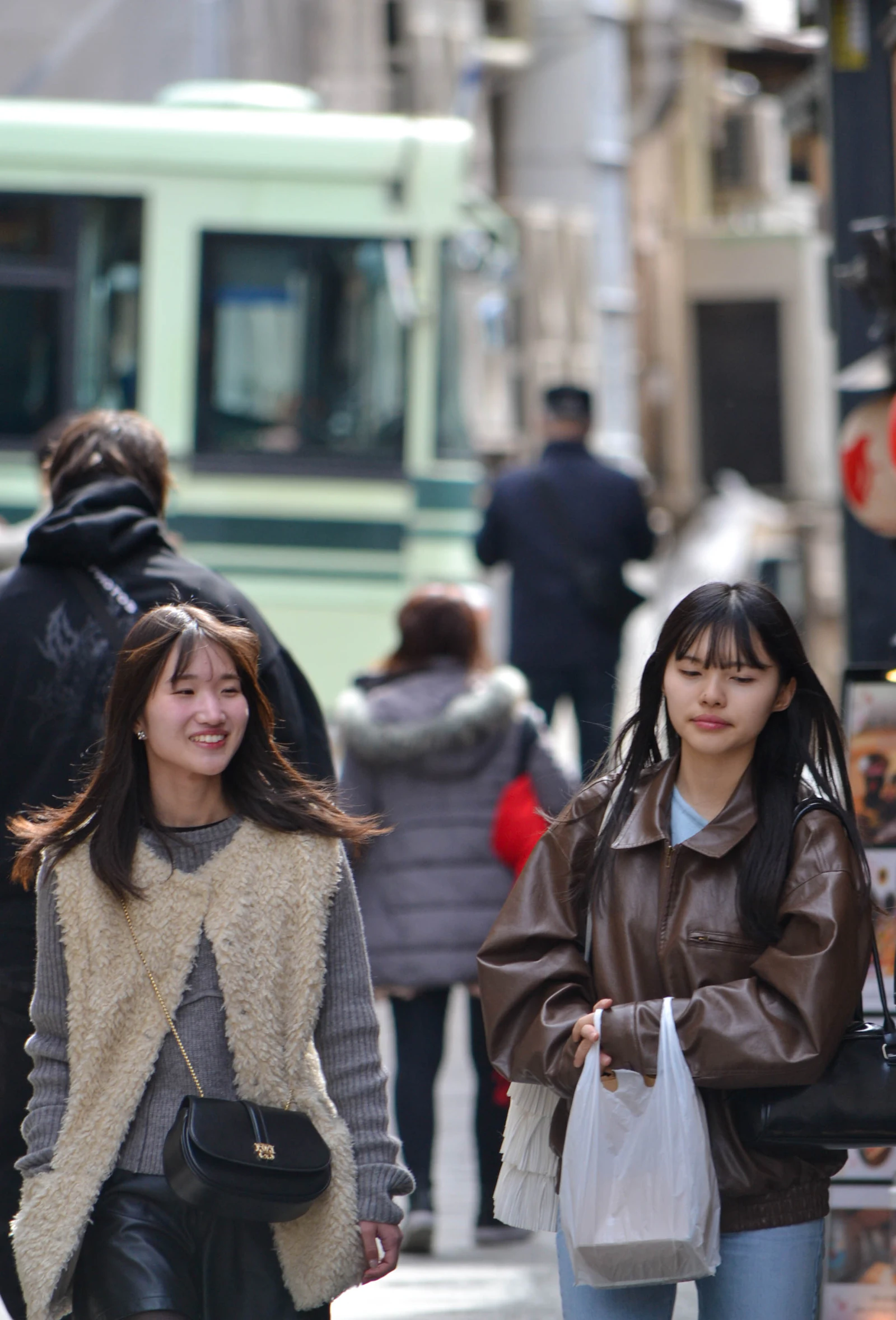 Two women walking down a busy city street in layered outfits