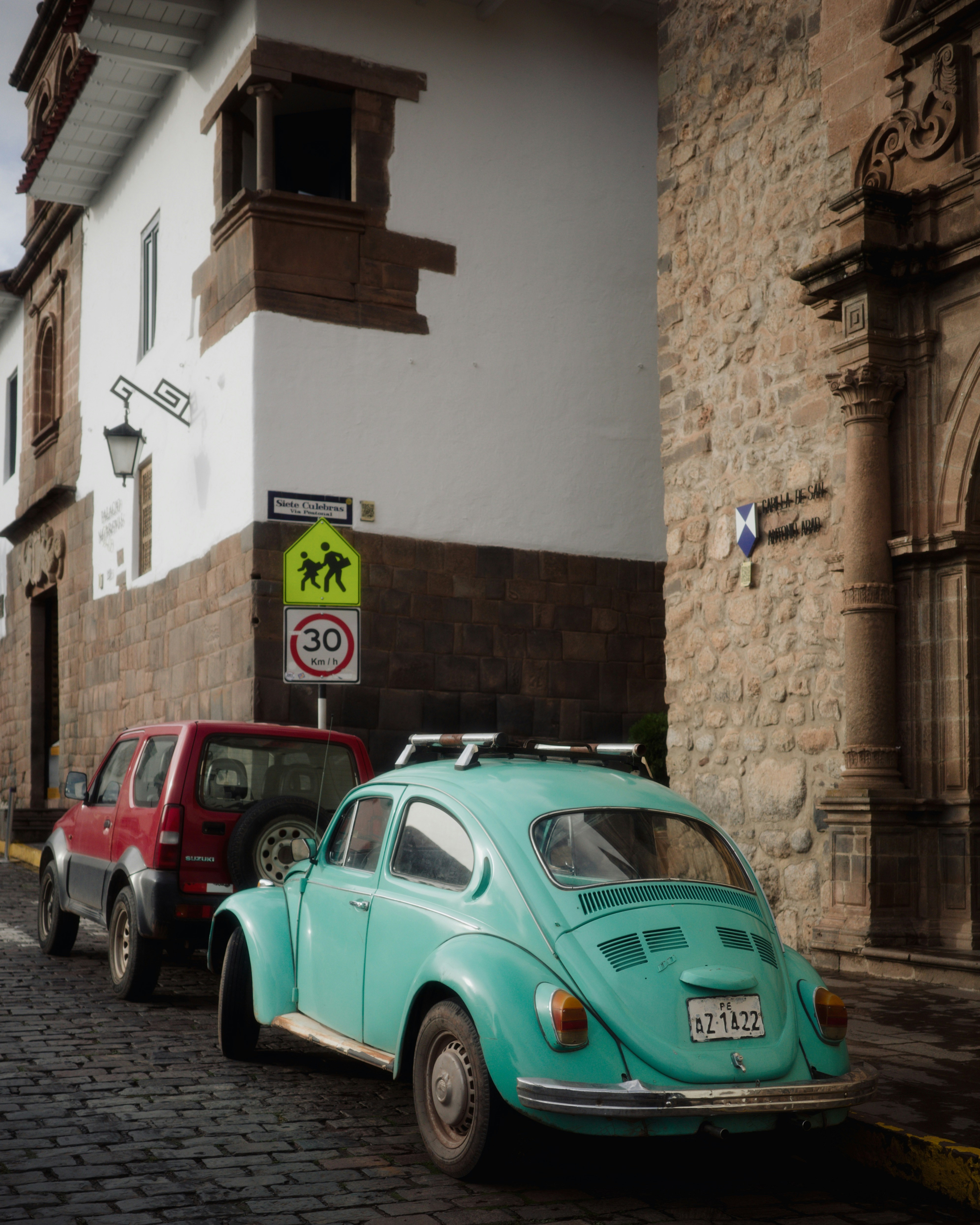 A teal volkswagen beetle parked on a cobblestone street.