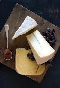 A board of cut cheeses with grapes and a small spoon, photographed from above