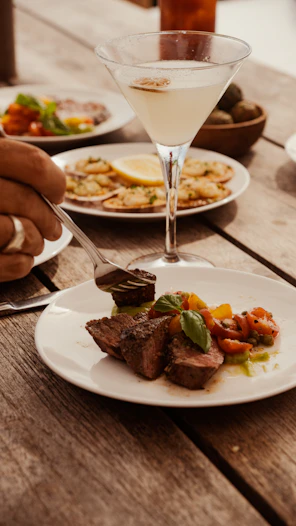 Steak and vegetables served with a martini on a table.