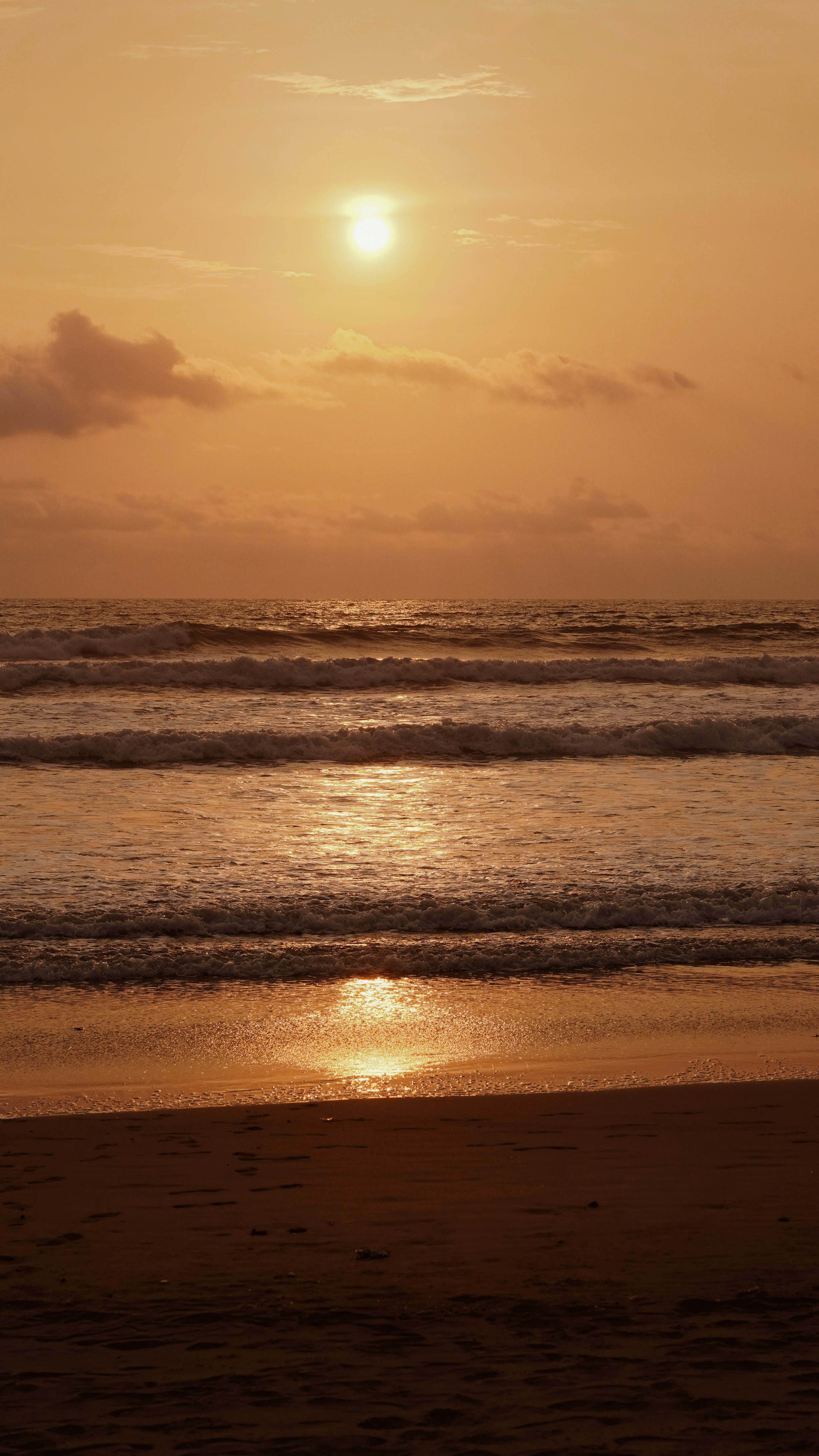 Sunset over the ocean with gentle waves on shore.