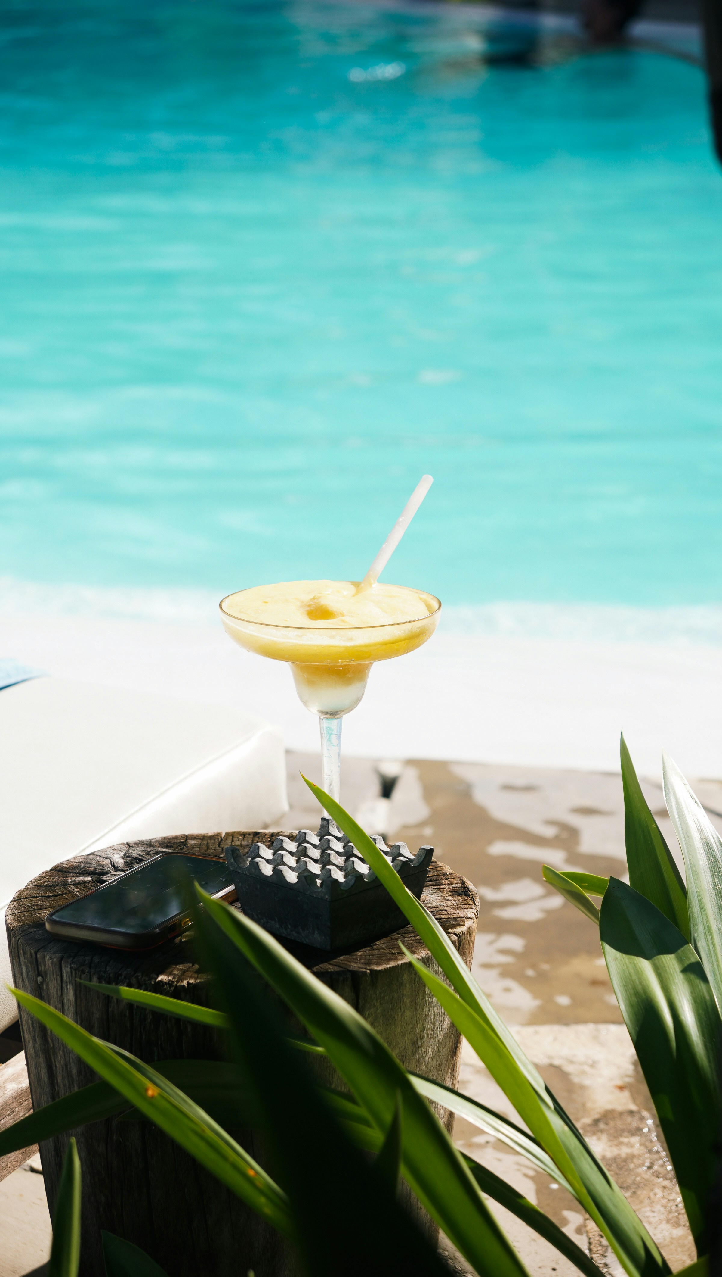 Frozen yellow cocktail with straw by pool
