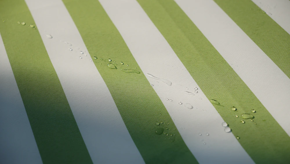 Gotas de água sobre tela de toldo às riscas verdes e brancas