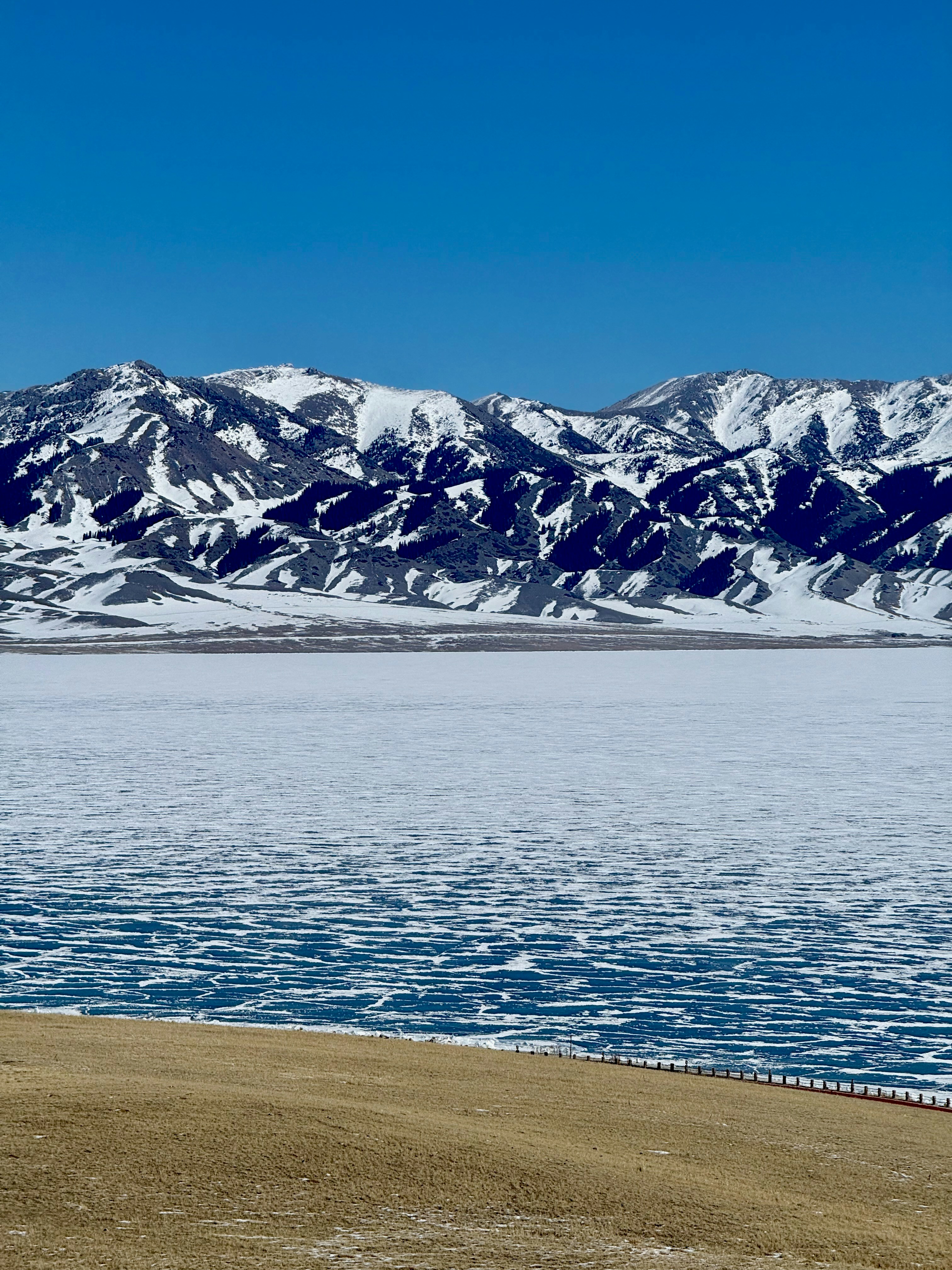 Snow-capped mountains overlook a frozen lake under a clear sky.