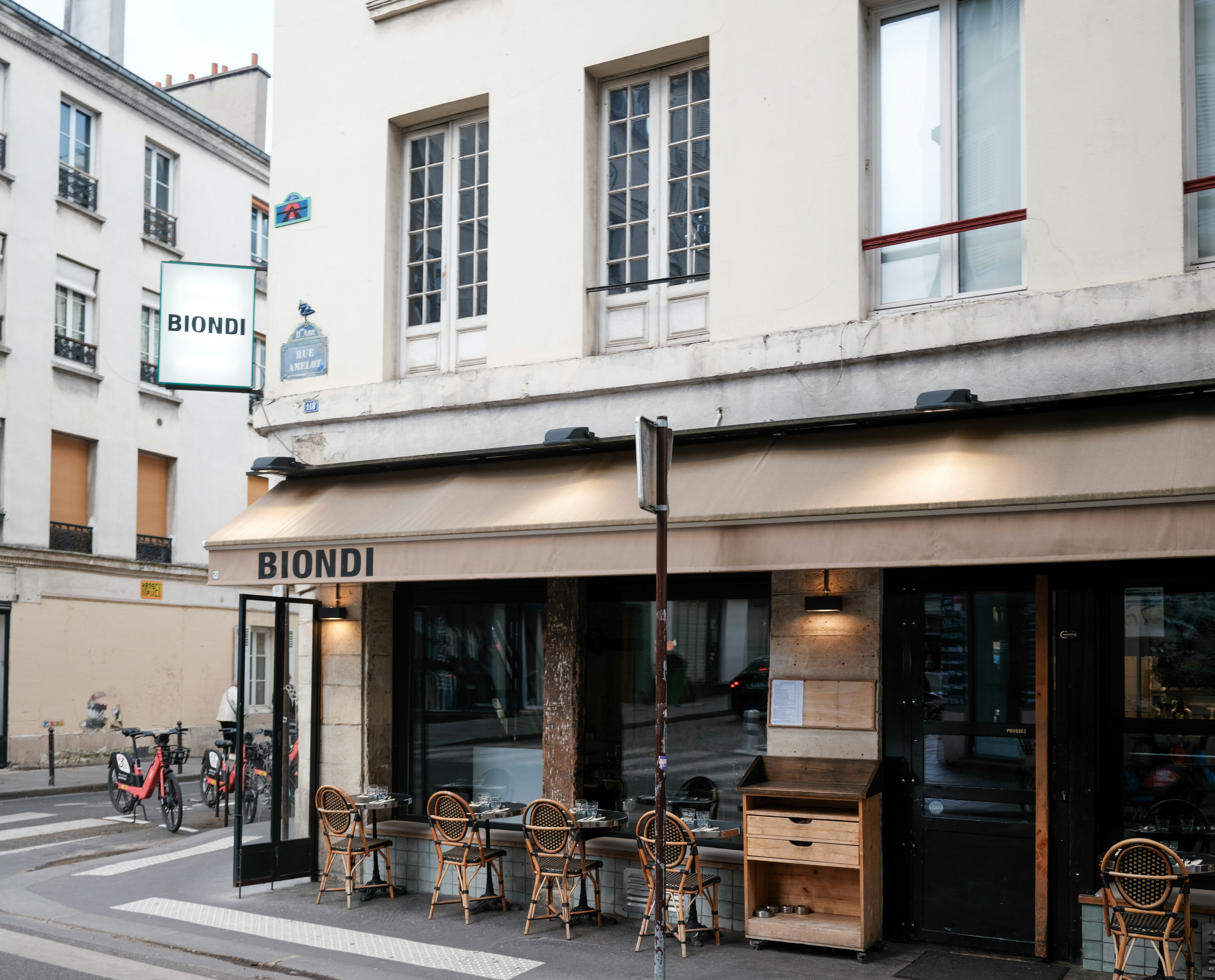 Um café parisiense com assentos ao ar livre e toldos.