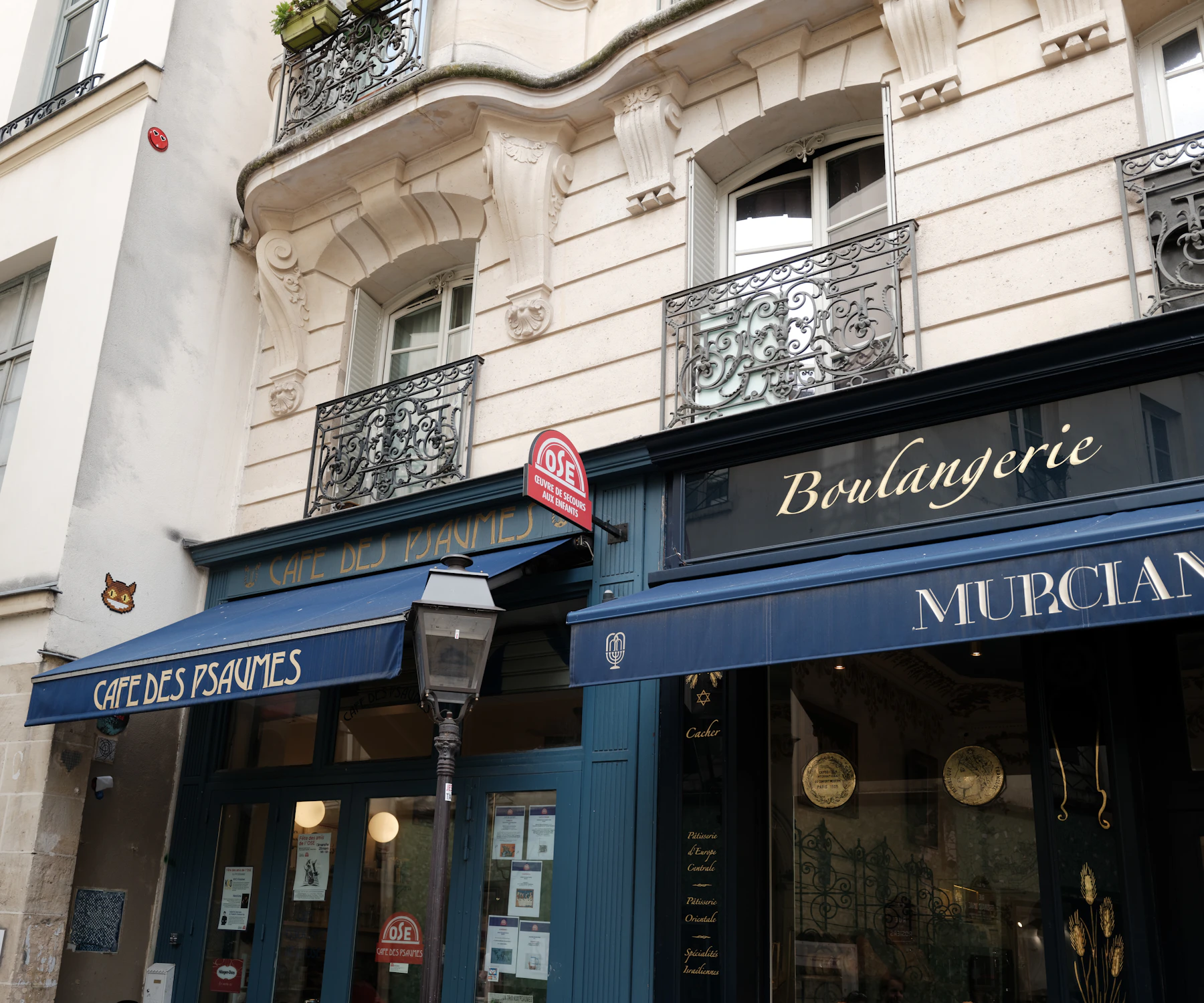 A Paris street corner with navy awnings, one lettered for a cafe and one for a boulangerie, under stone balconies