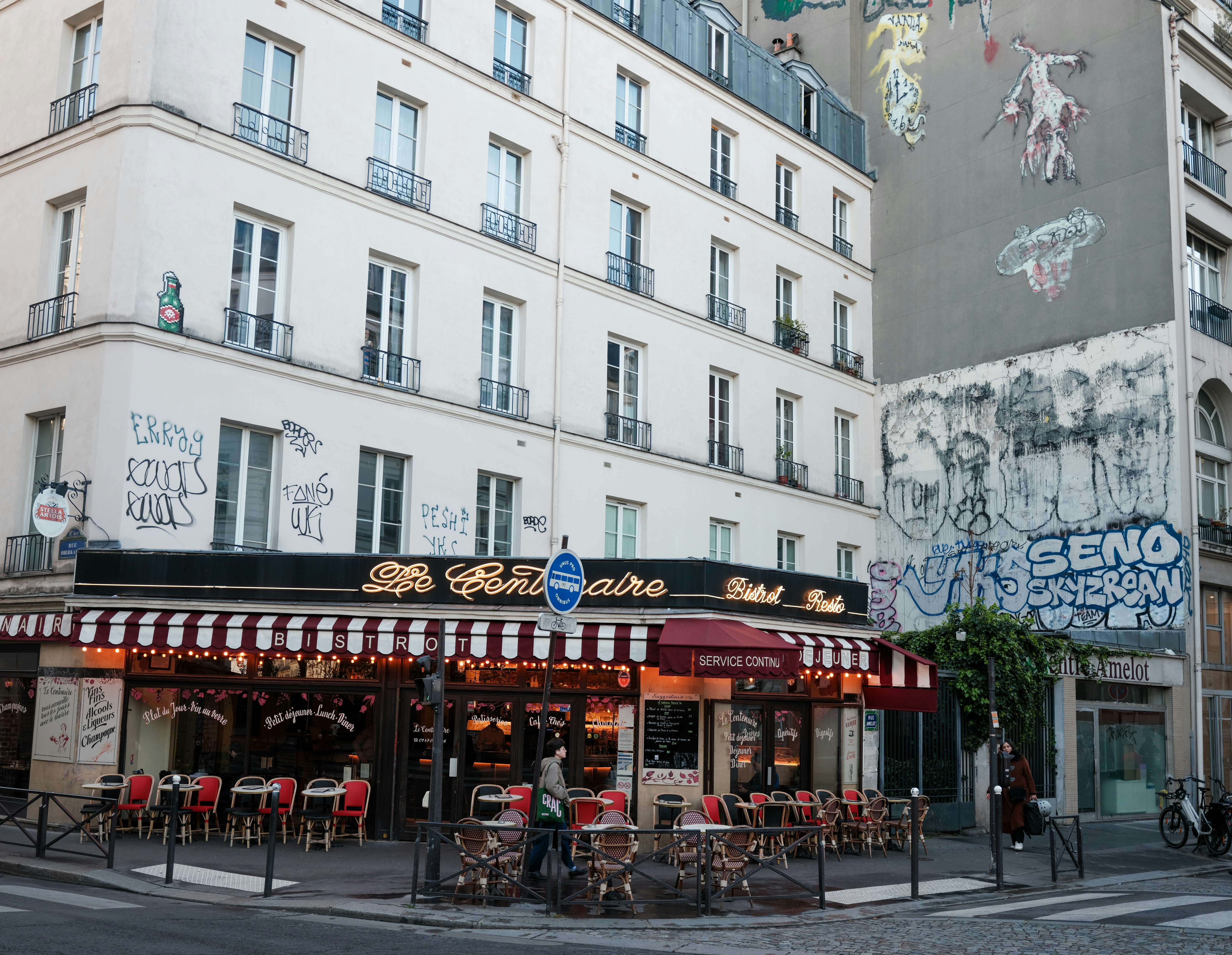 A parisian cafe with outdoor seating and graffiti on buildings.