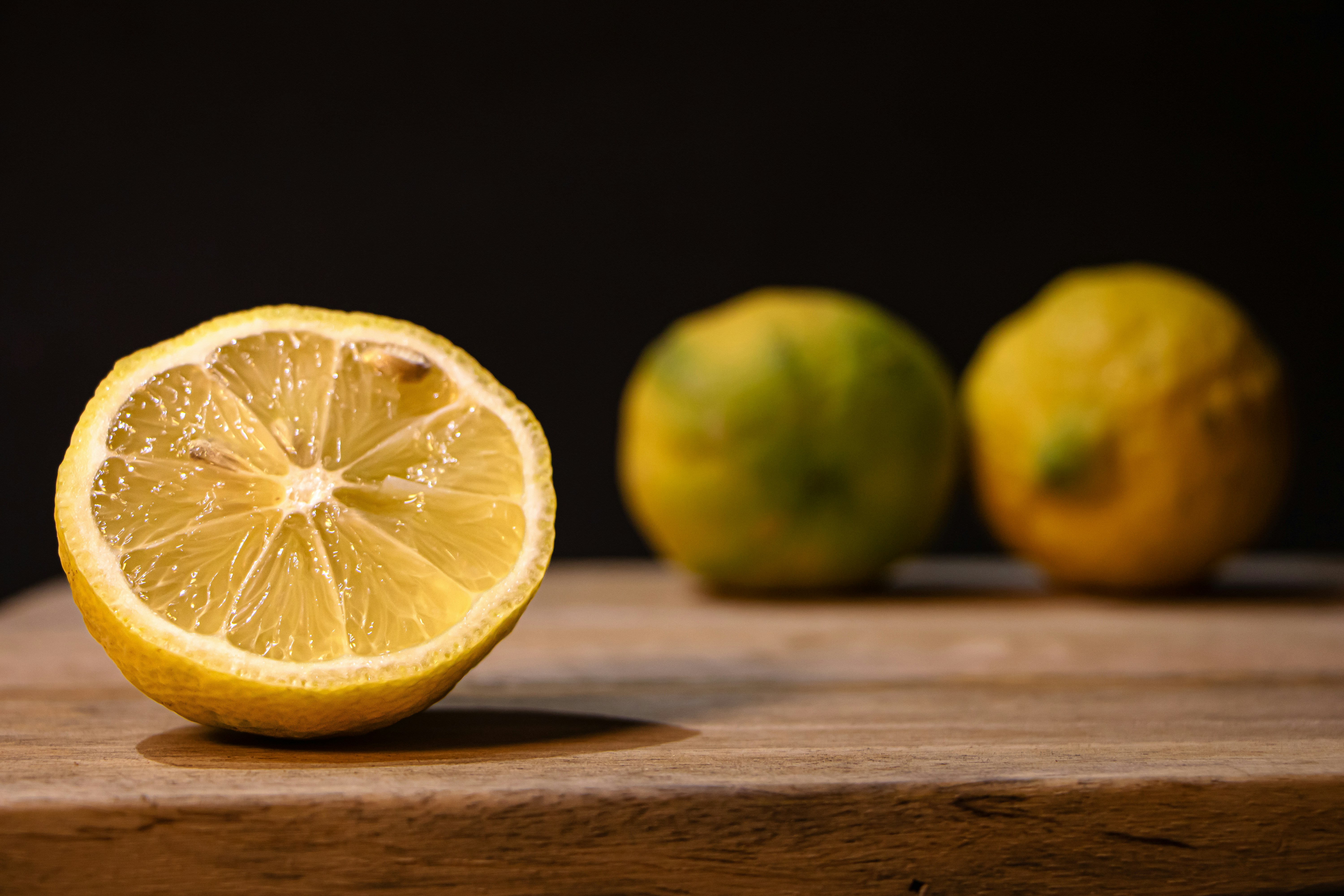 A halved lemon with two whole lemons behind it.