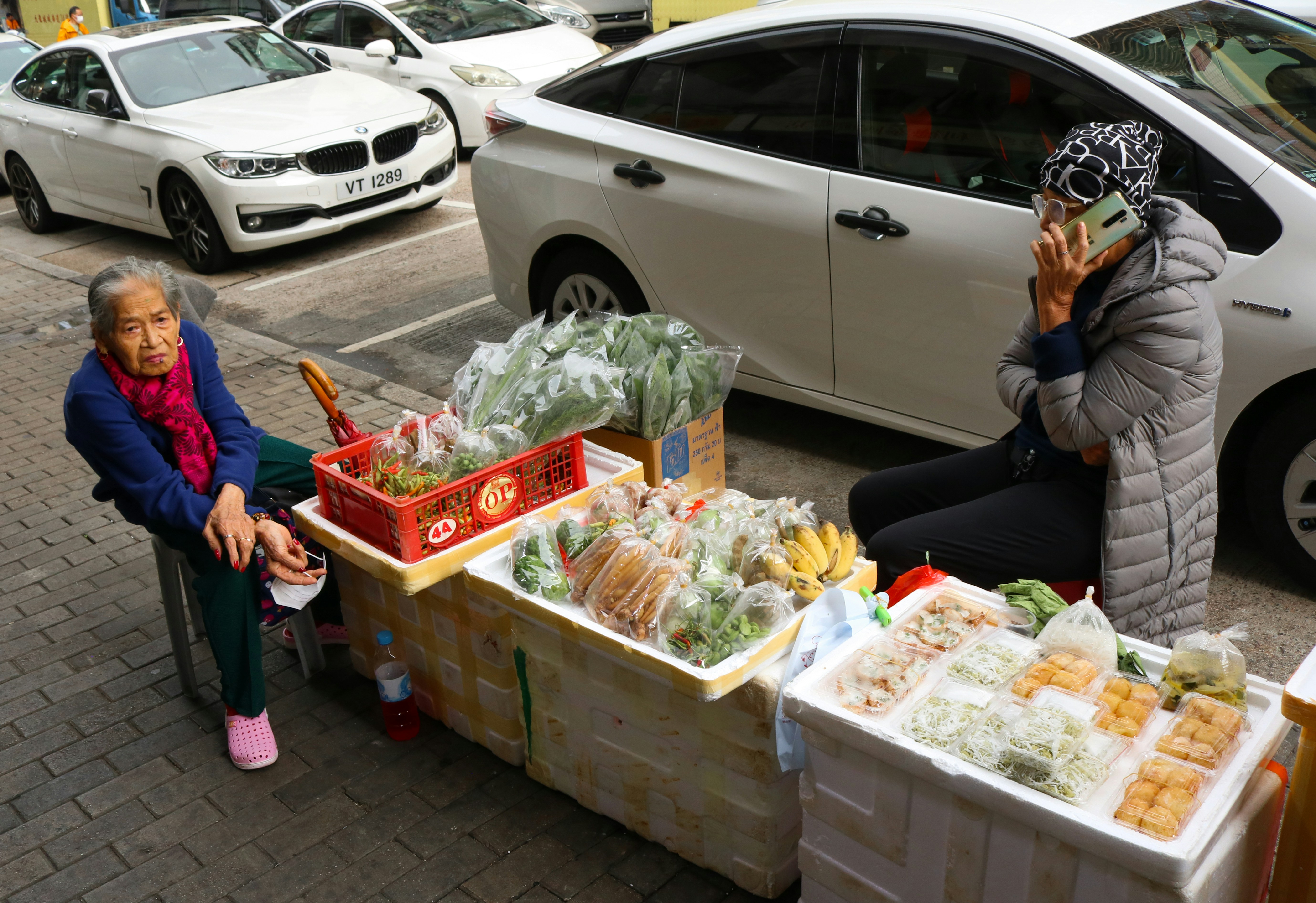 Two elderly women selling produce from carts on a street.