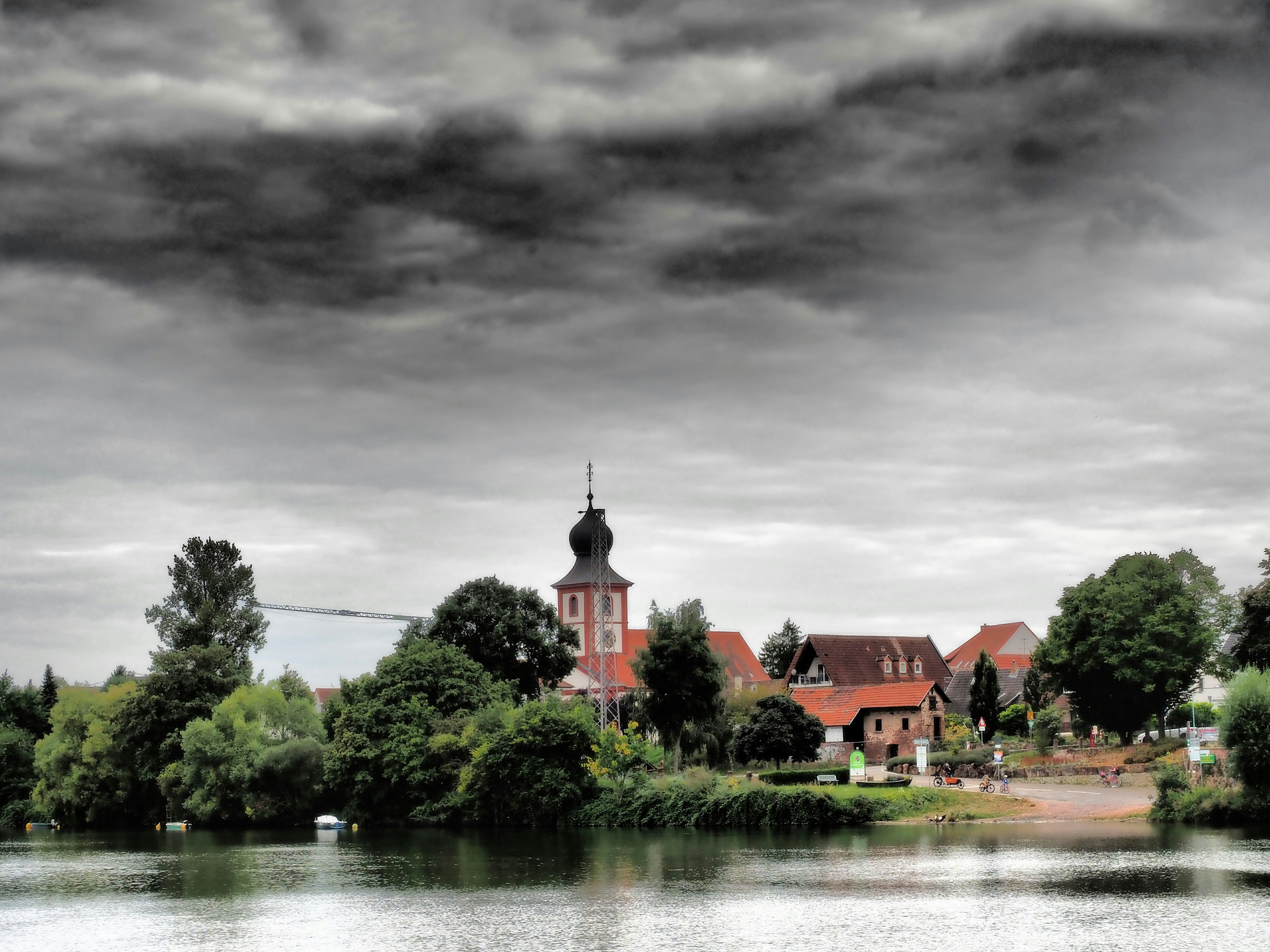 Village with church steeple by a lake under stormy skies