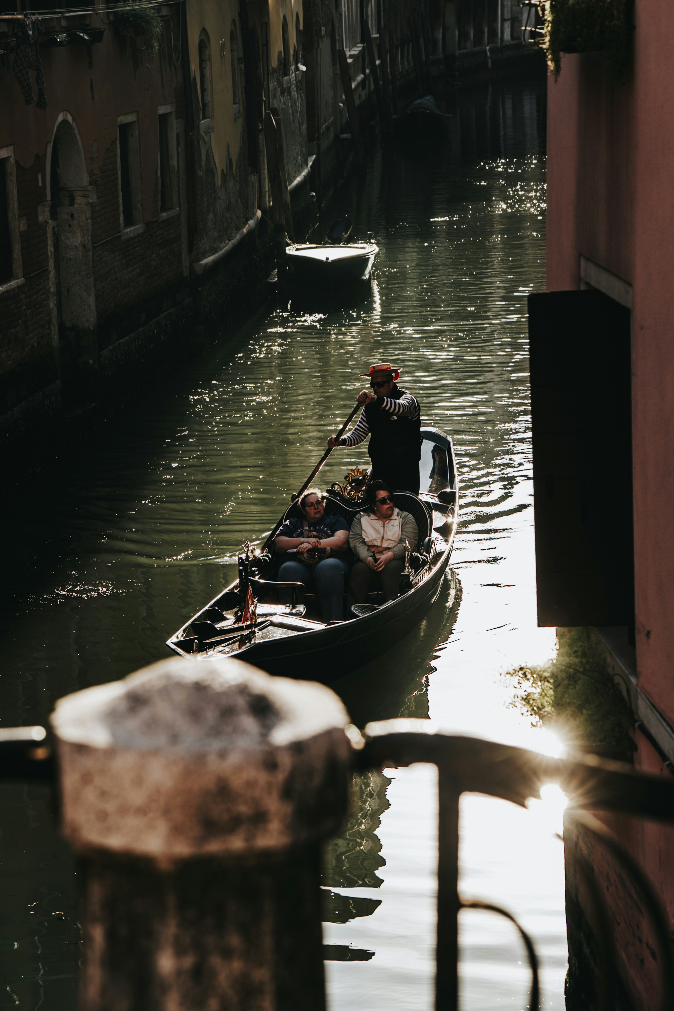 Gondola with tourists navigating a narrow venetian canal.