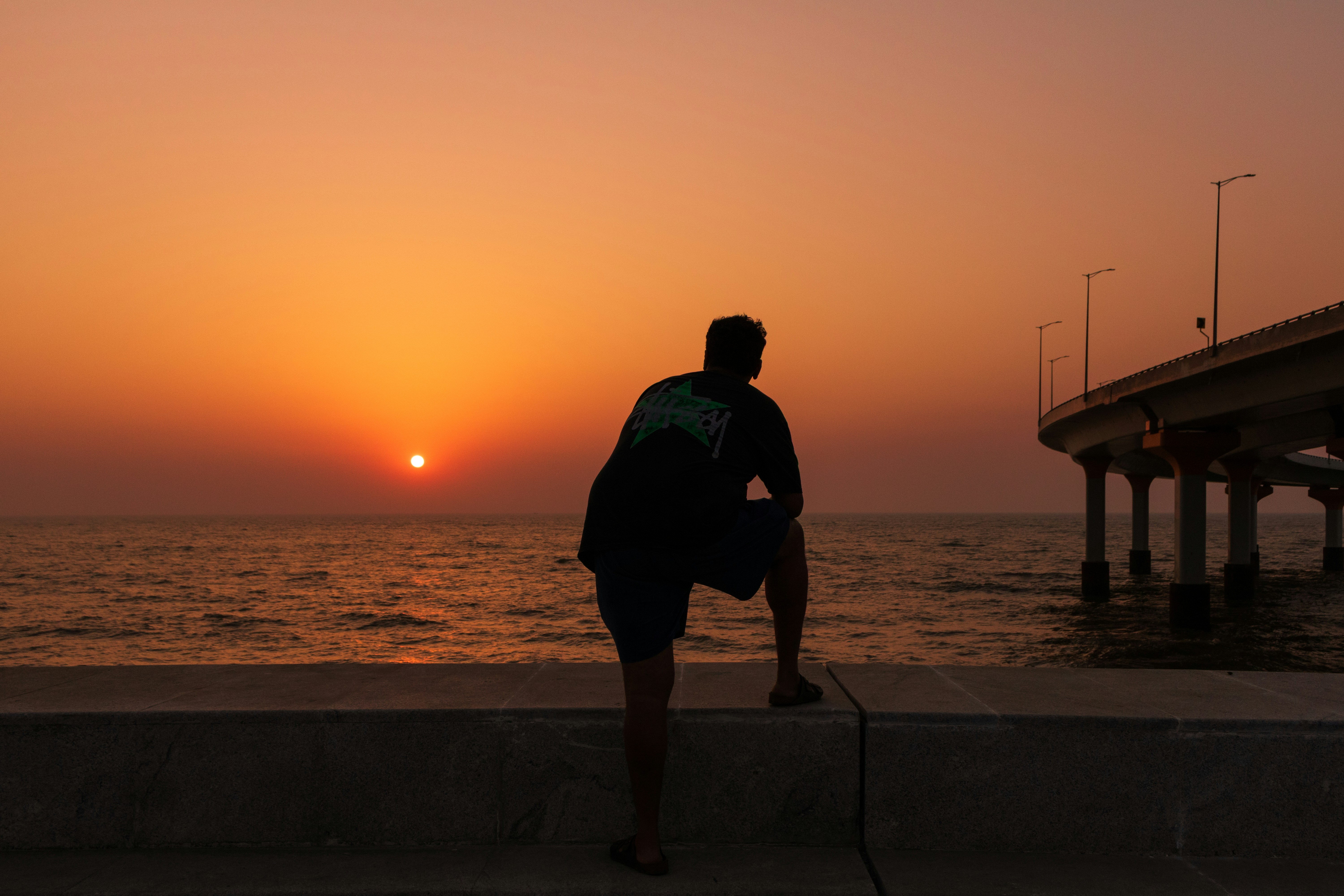 Man watches sunset over the ocean from a pier.