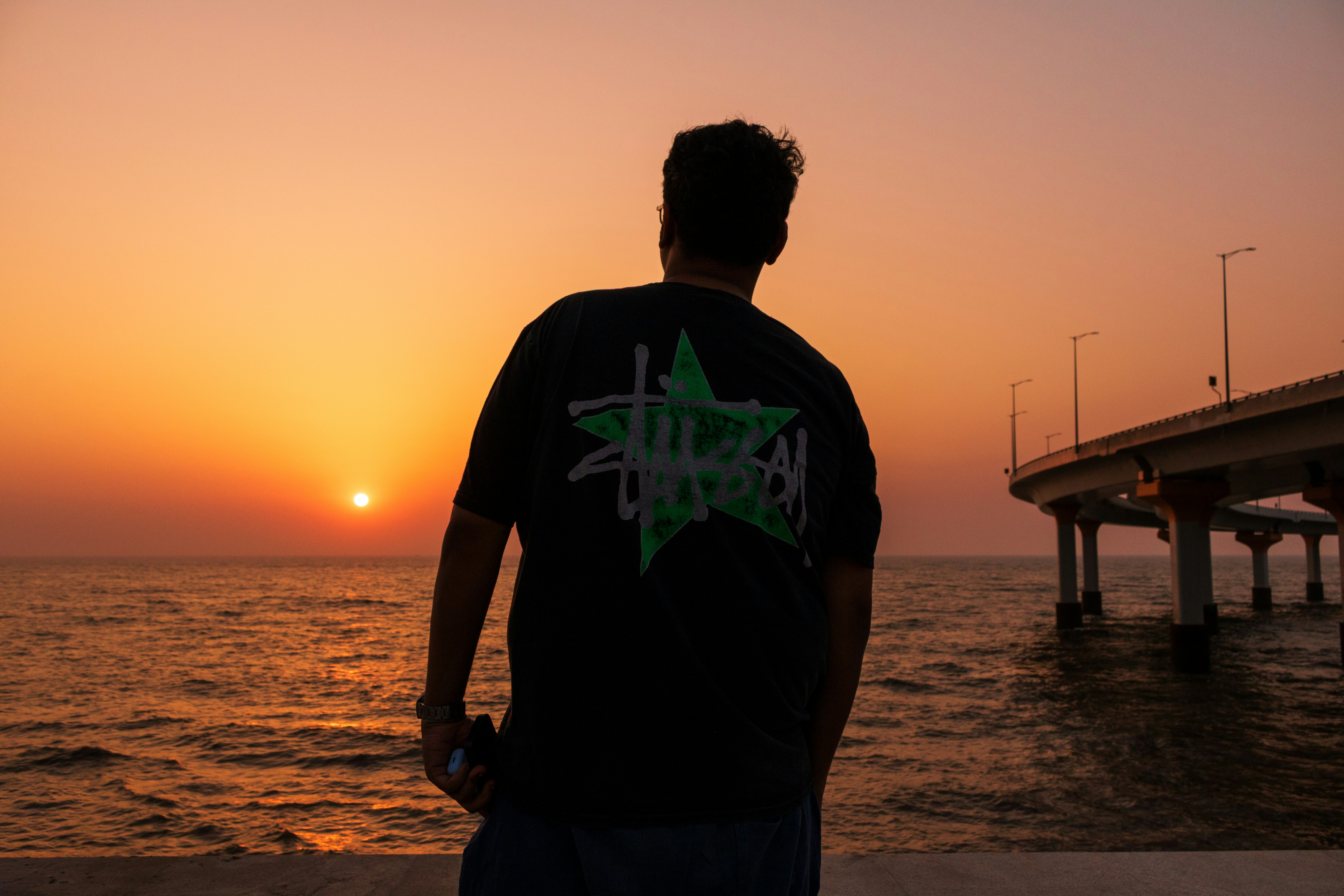 Man watching sunset over the ocean near a bridge