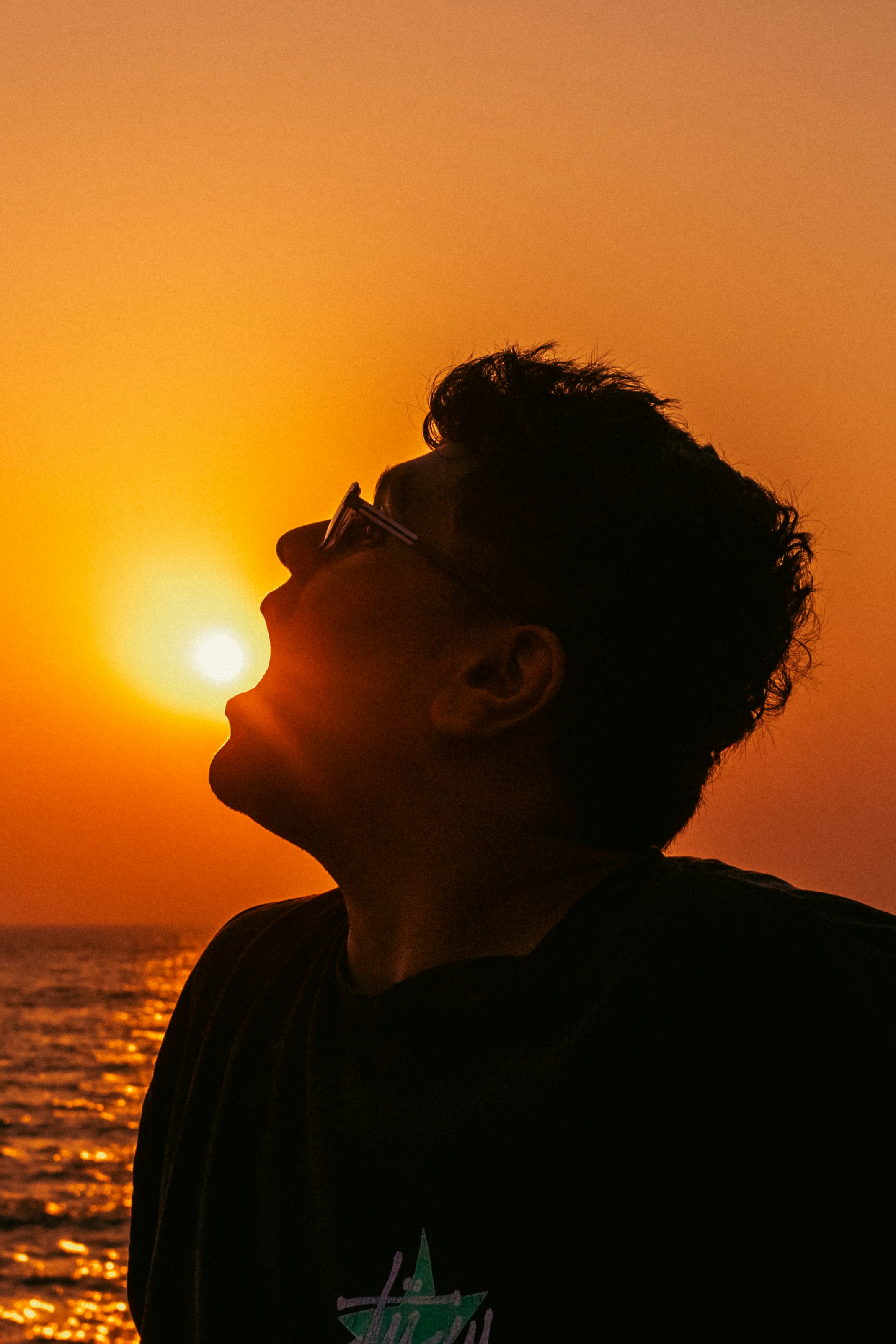 Man with mouth open silhouetted against sunset over ocean