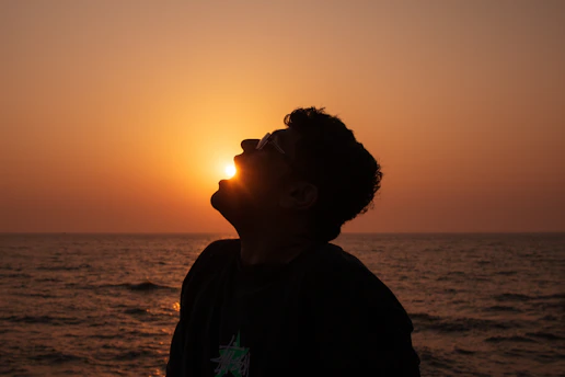 Silhouette of a man with sun setting over the ocean.